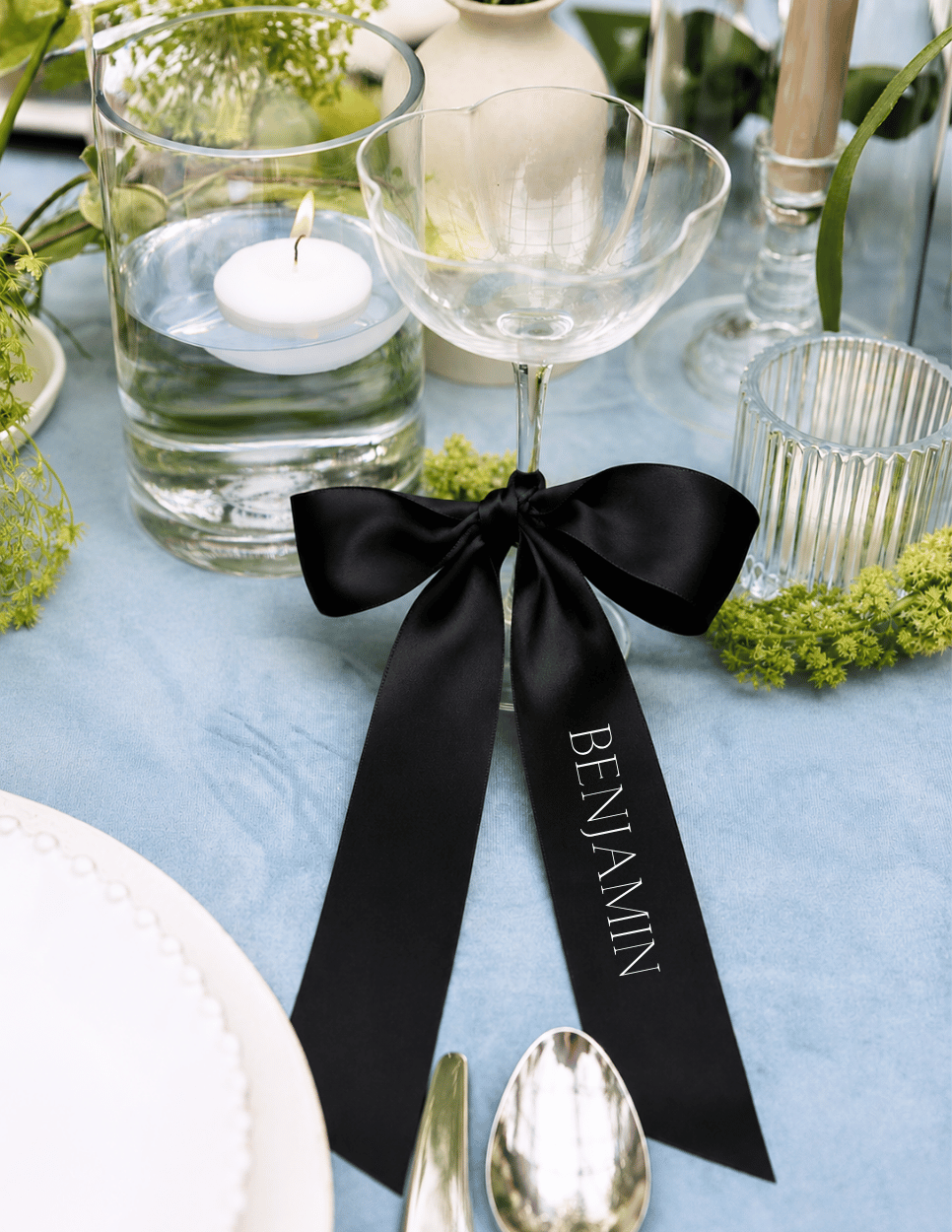 Personalized black satin ribbon place card on a champagne glass for an elegant wedding reception table setting.