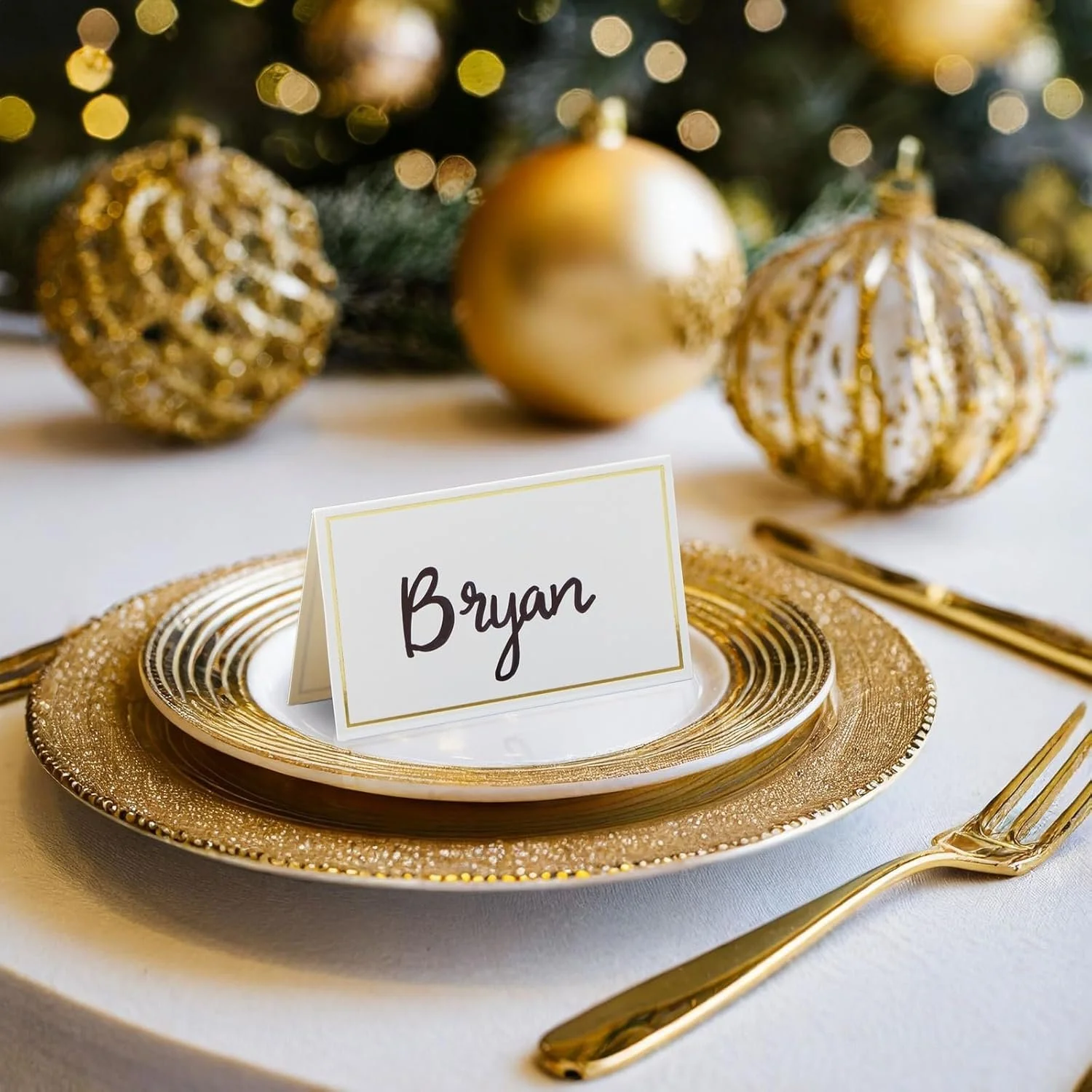 White cardstock place card with gold trim around personalized with a guest’s name in gold lettering for an elegant wedding reception table setting.
