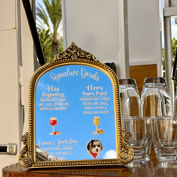 Decorative sign displaying signature drinks at a cafe, with descriptions and illustrations of drinks, alongside empty water glasses on a table.