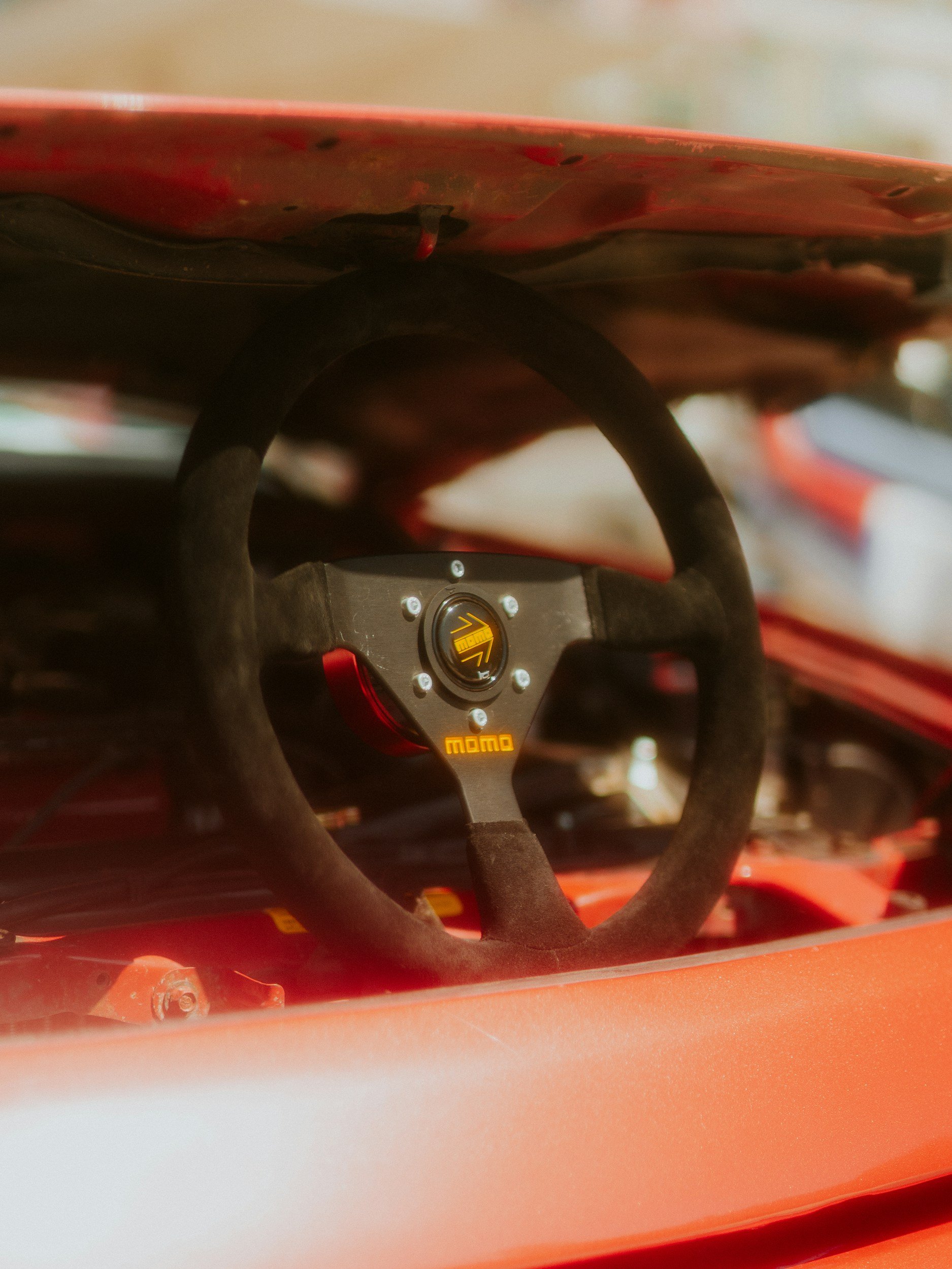 Close-up of a racing car's black steering wheel with Momo logo, set inside a drift car cockpit.