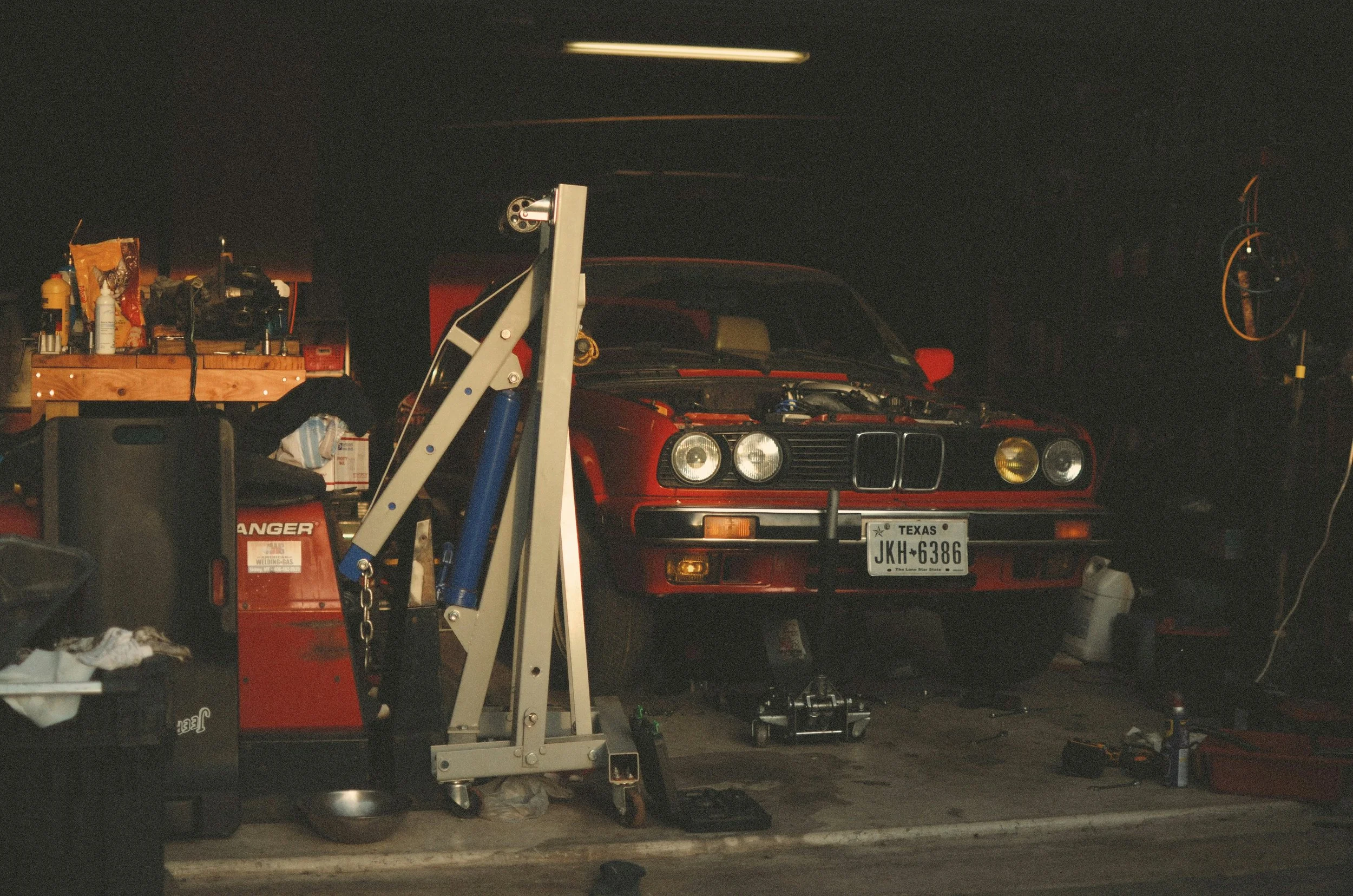 Red BMW parked in a garage surrounded by tools and equipment, with a license plate indicating Texas