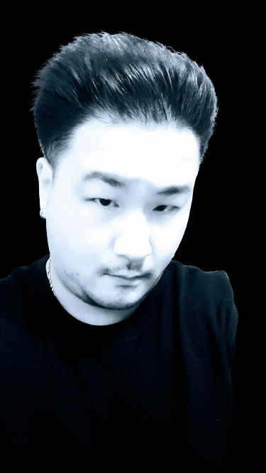 Black and white portrait of a young man with styled hair, wearing a black shirt, against a dark background.
