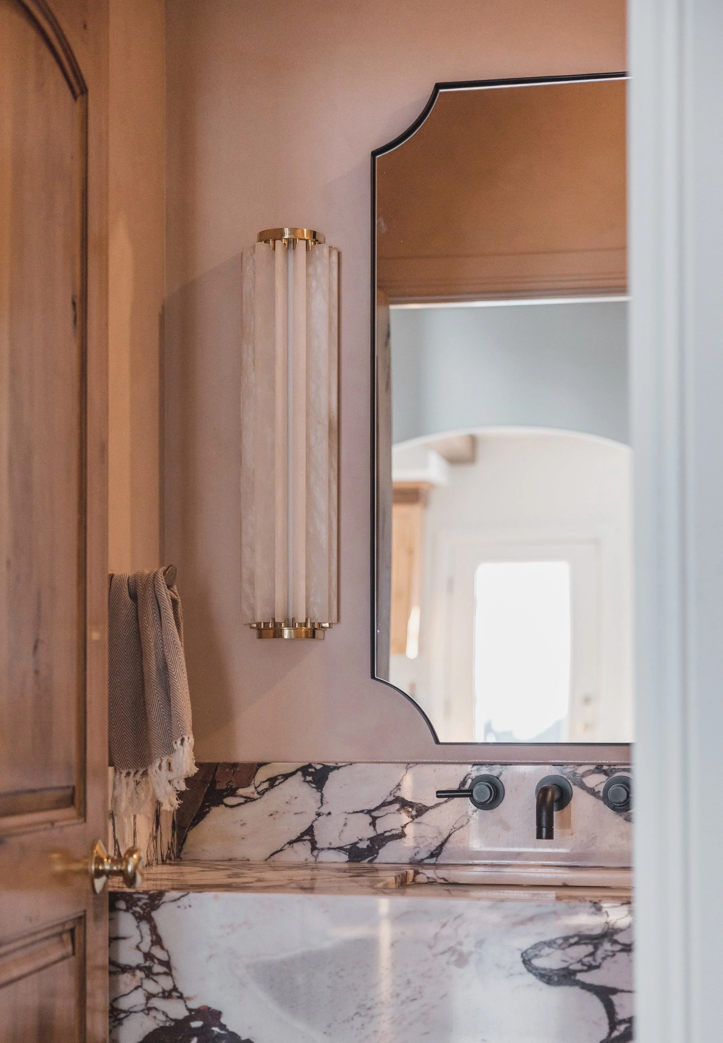 A bathroom vanity with a marble countertop, a large mirror, and wall-mounted light fixture.