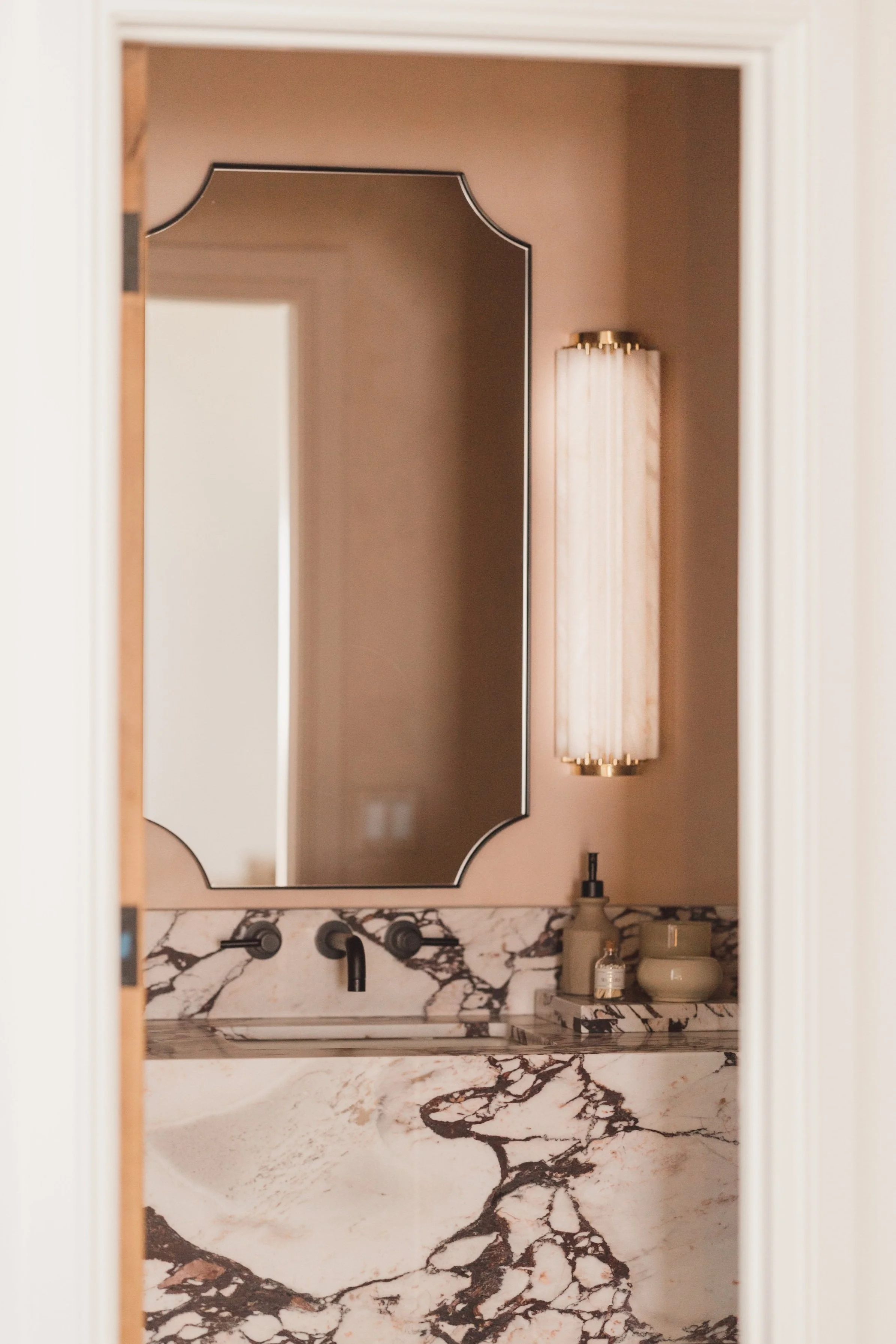 A bathroom mirror with a marble countertop and a tall wall-mounted light fixture.