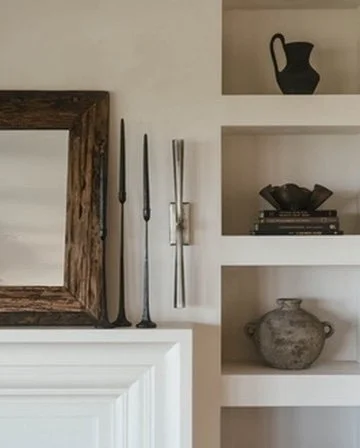 White built-in bookshelf with decorative items and a mirror with a wooden frame on the left side.
