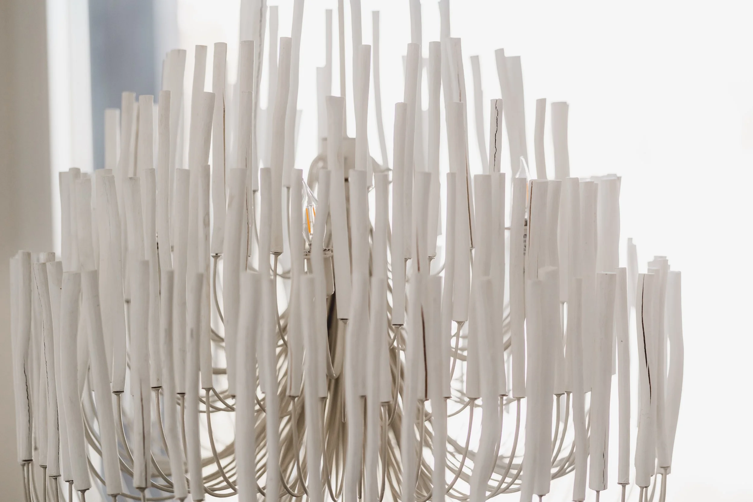 Close-up of a white decorative light fixture with multiple elongated candle-like elements and small visible light bulbs, backlit by natural light.