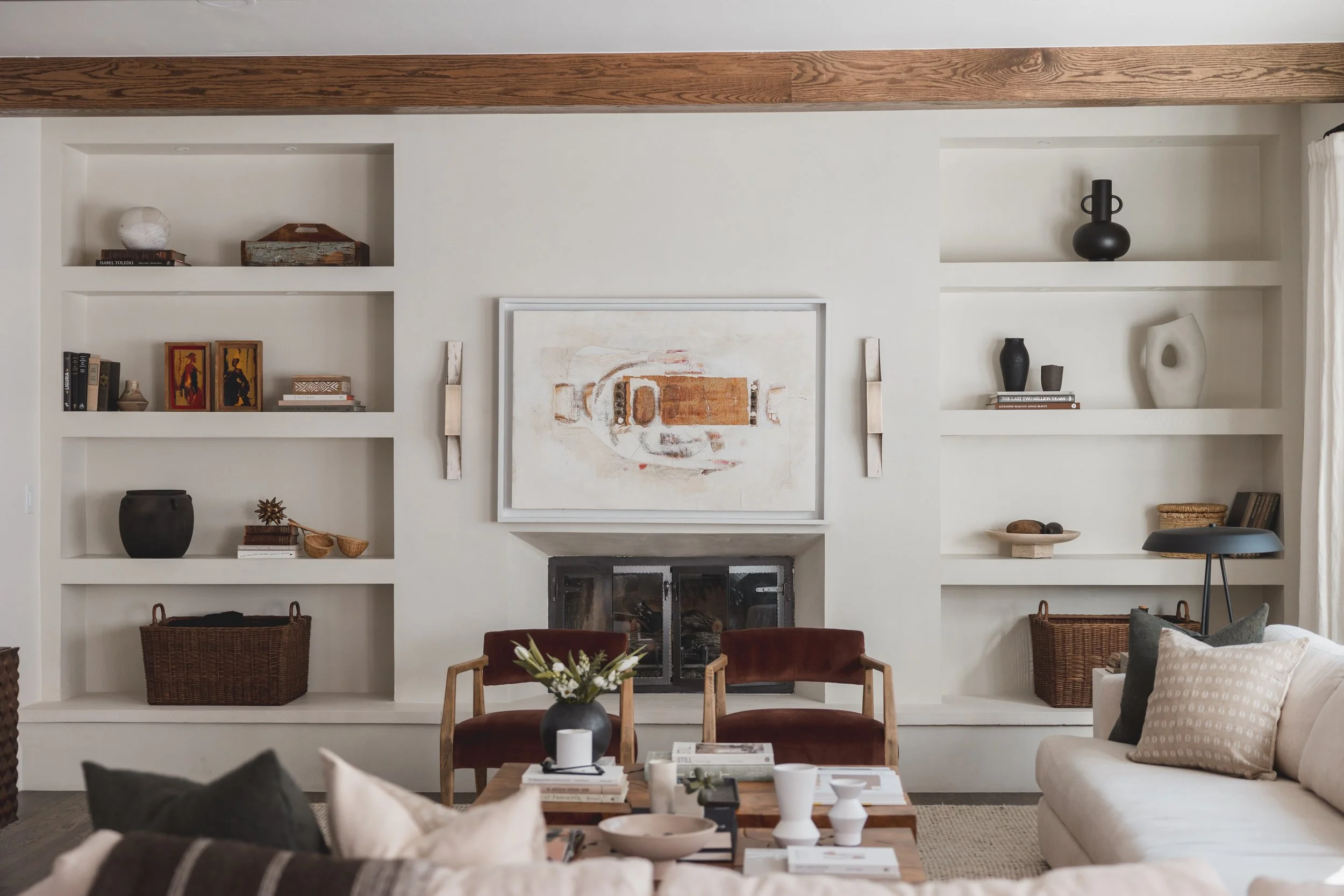 Living room with a white fireplace, built-in shelves with decorative objects, and sitting area with beige and brown furniture.