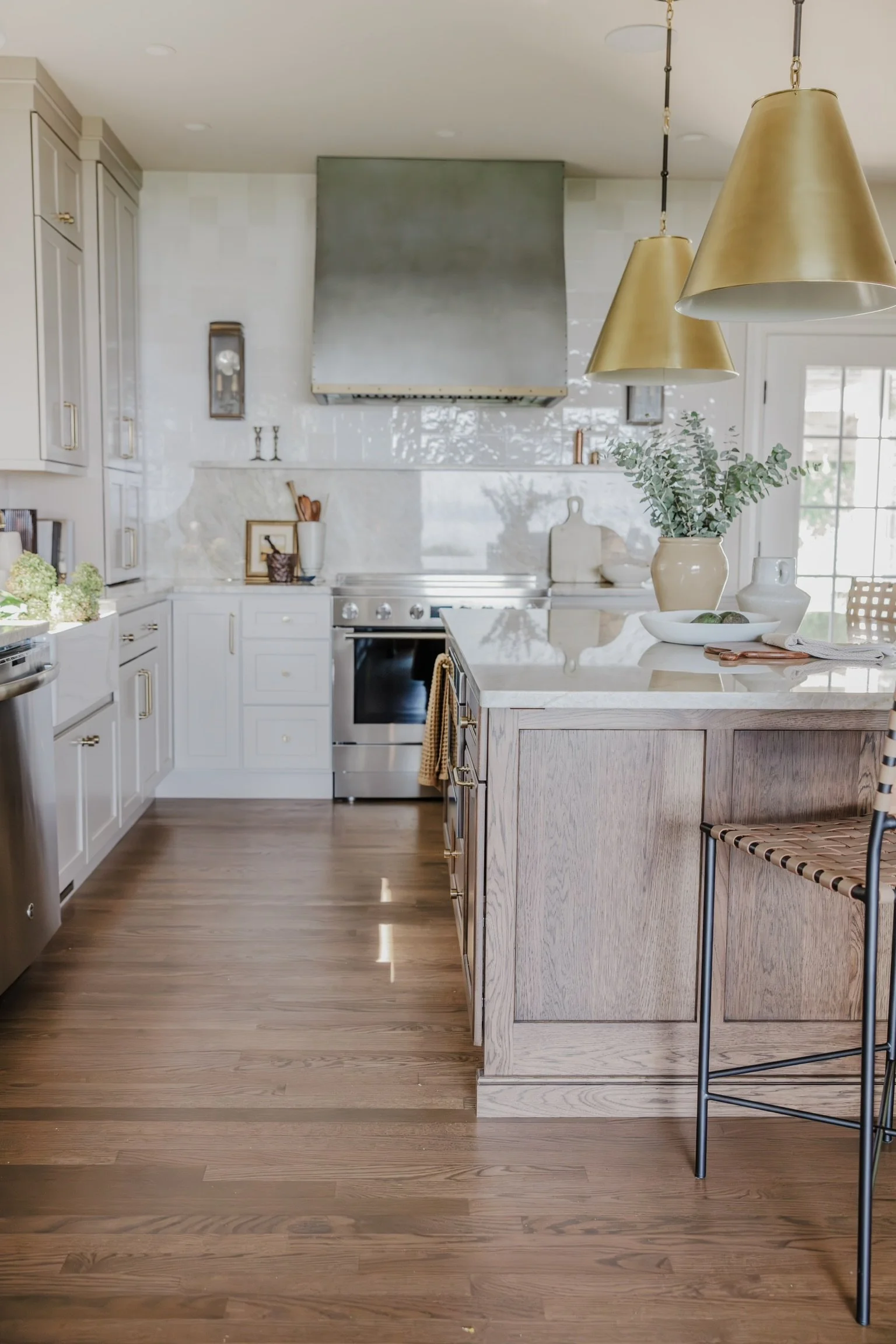 Modern kitchen with white cabinets, a central island with wood finish, gold pendant lights, a stainless steel range, and wooden flooring.