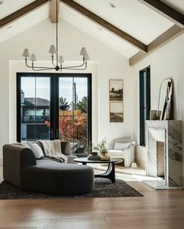 Living room with large sliding glass doors, a gray sectional sofa, a coffee table, and fireplace with a mirror above, decorated in neutral colors.