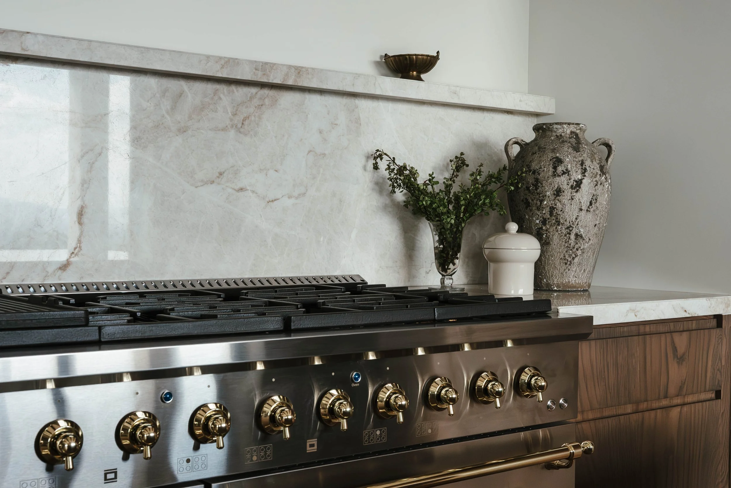 Kitchen counter with decorative vases, a glass with greenery, and a stove with gold knobs.