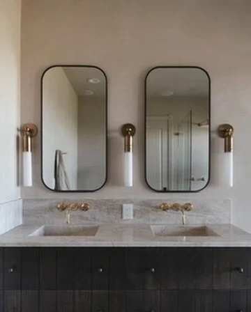 Bathroom with two rectangular mirrors above a double sink vanity with gold fixtures, beige wall, and dark cabinet