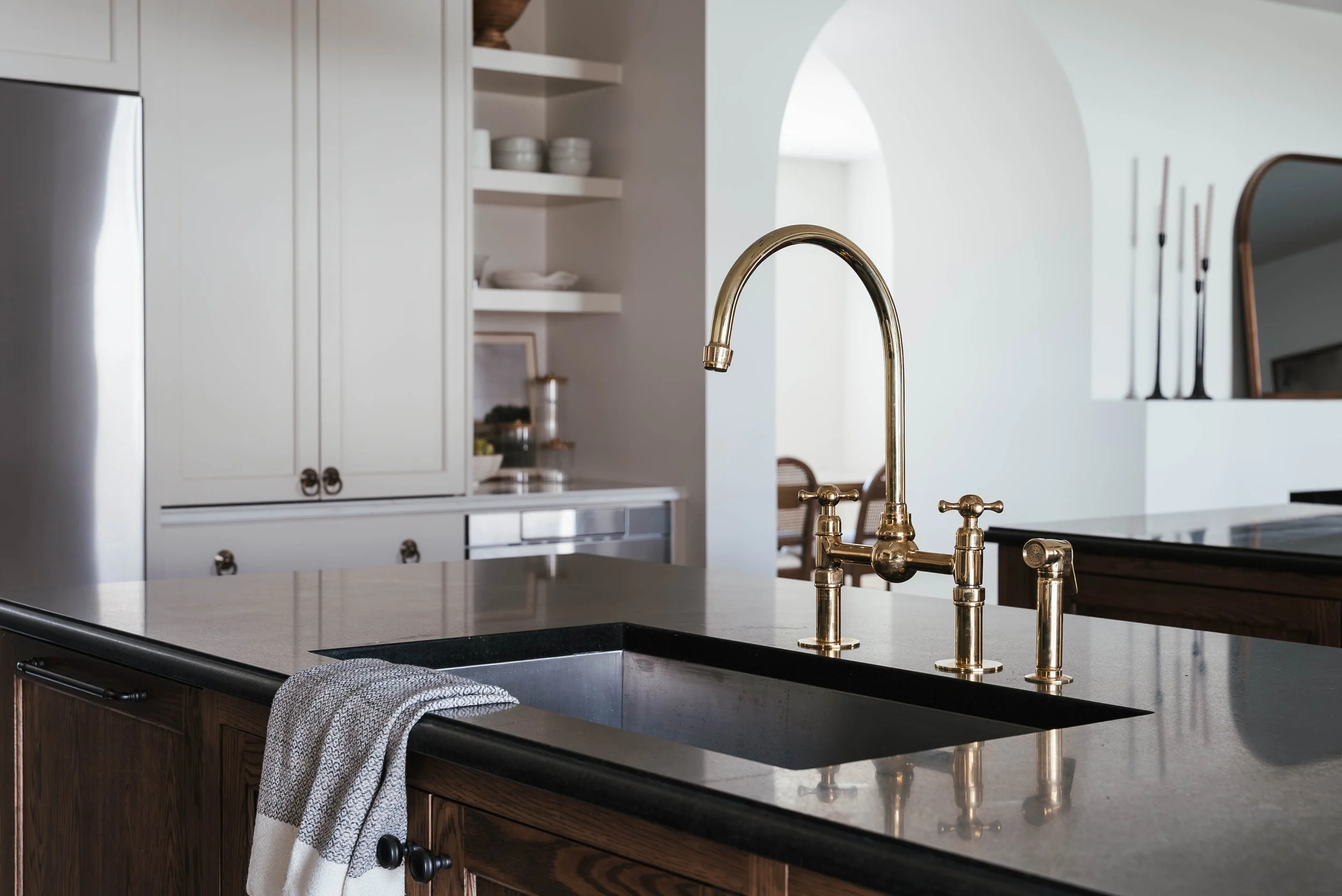 A kitchen with a black stone countertop, a brass faucet above a sink, and white cabinets in the background.