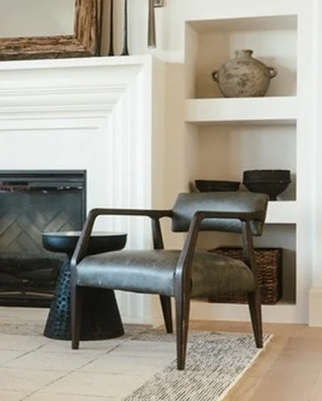 Living room corner with a fireplace, a black chair, a small side table, and built-in shelves with a decorative vase and bowls.