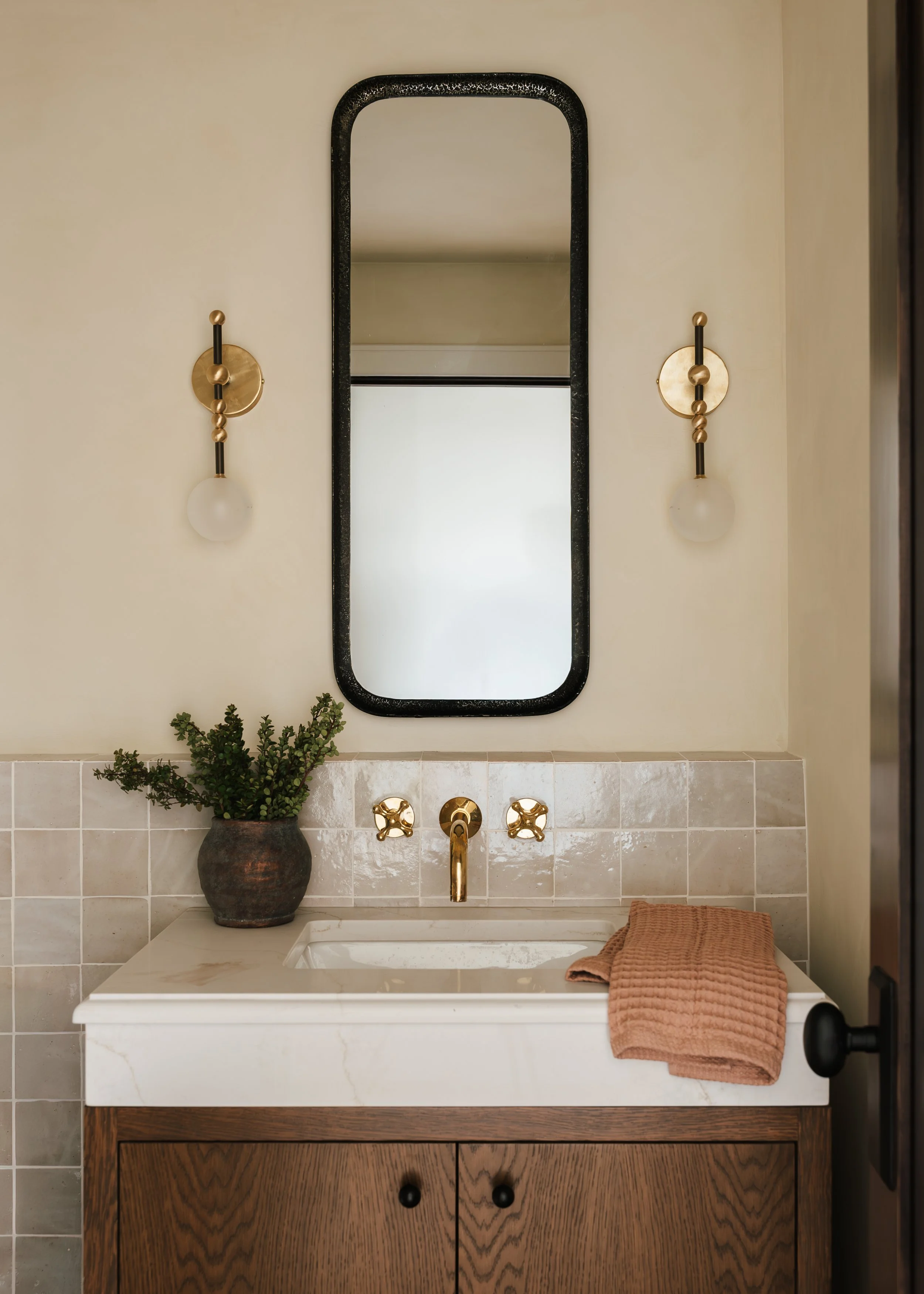 Bathroom vanity with a rectangular sink, a potted plant, a folded brown towel, a mirror, and wall-mounted light fixtures.
