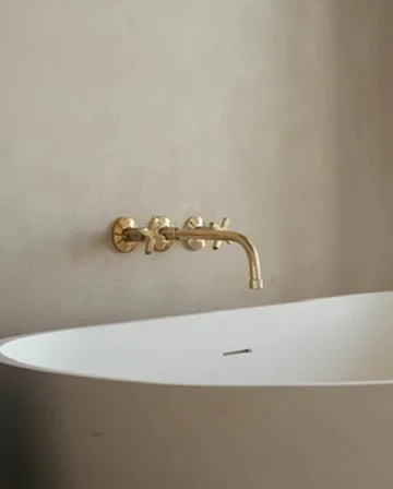 A gold-colored faucet mounted on a beige wall above a white sink with a flat edge.