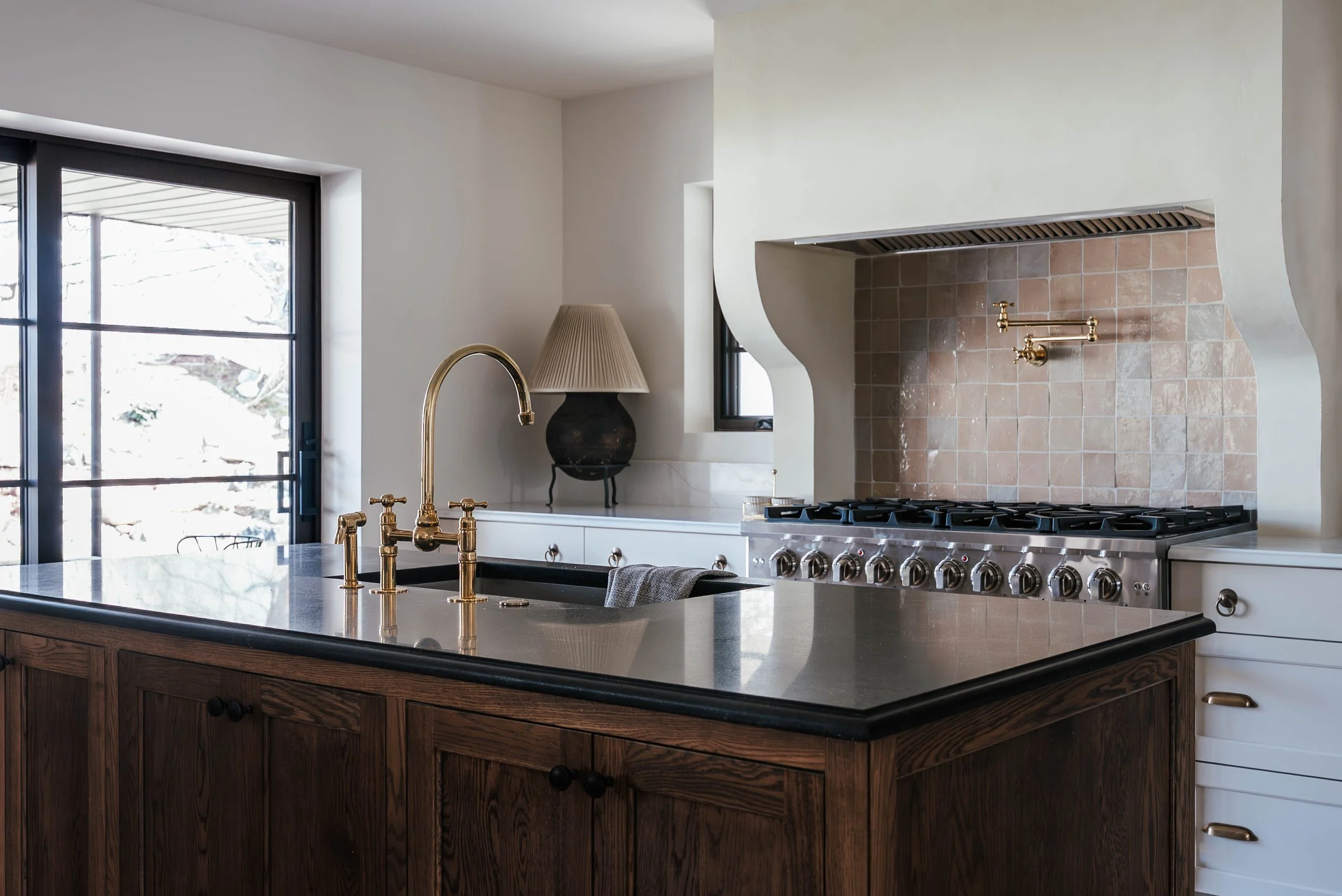 Modern kitchen with dark wood island, brass faucet, white cabinets, and a stainless steel stove with a brick backsplash.