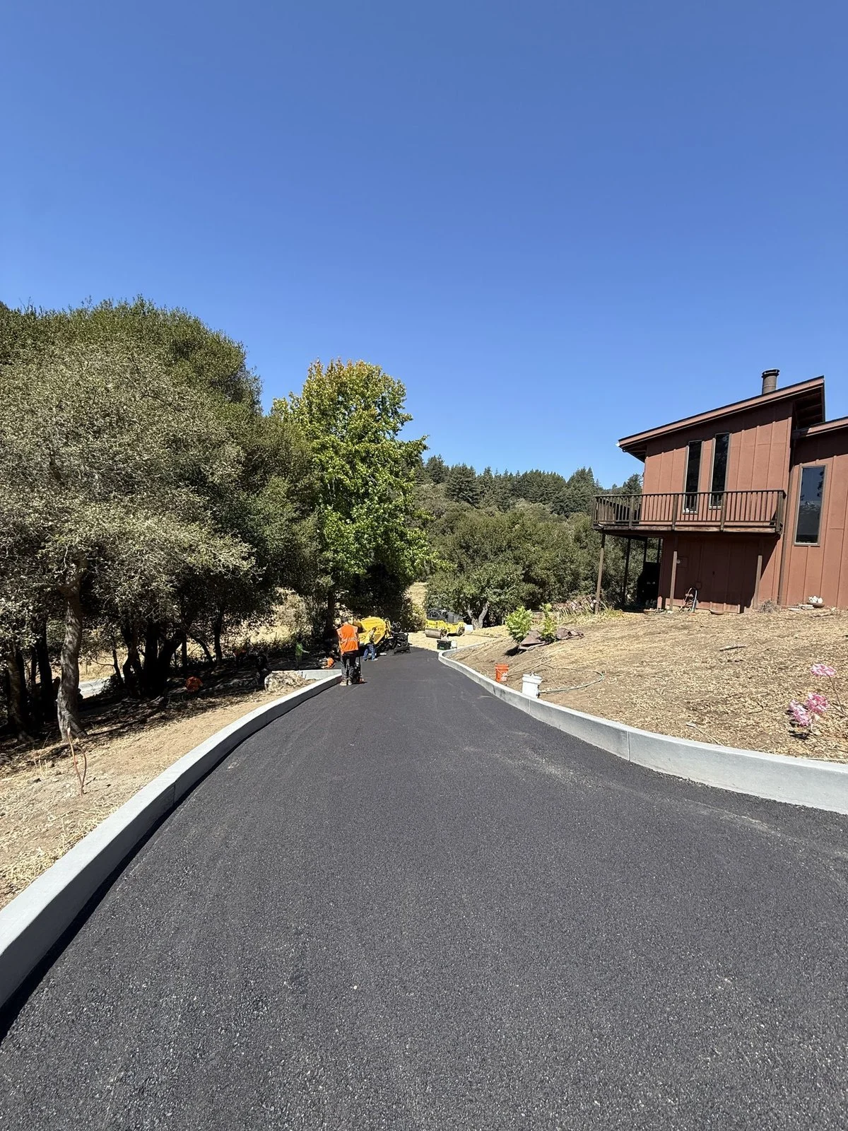 New asphalt driveway with concrete curbs on both edges to control water runoff