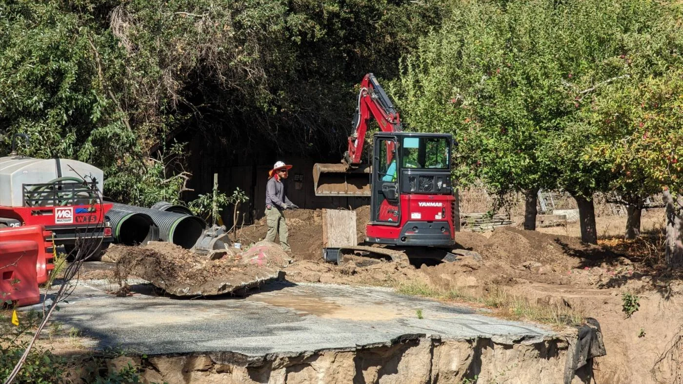 Crew member and red mini excavator digging on a residential job site