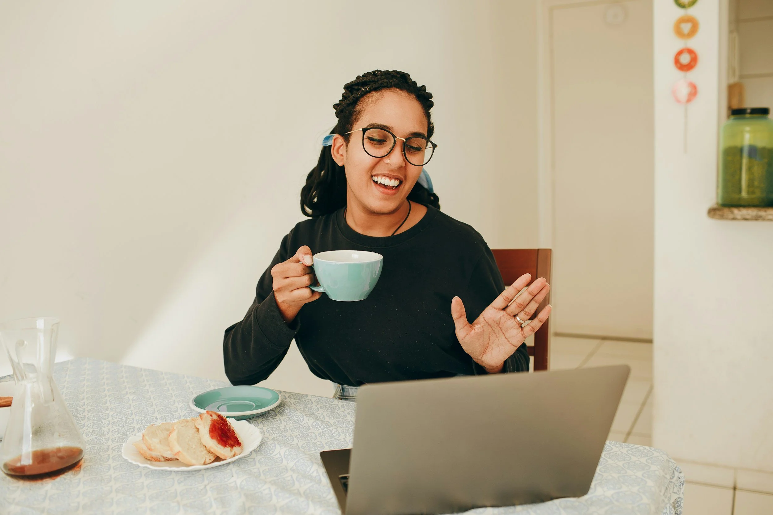 woman with dark hair holding a coffee cup waiving at her laptop screen