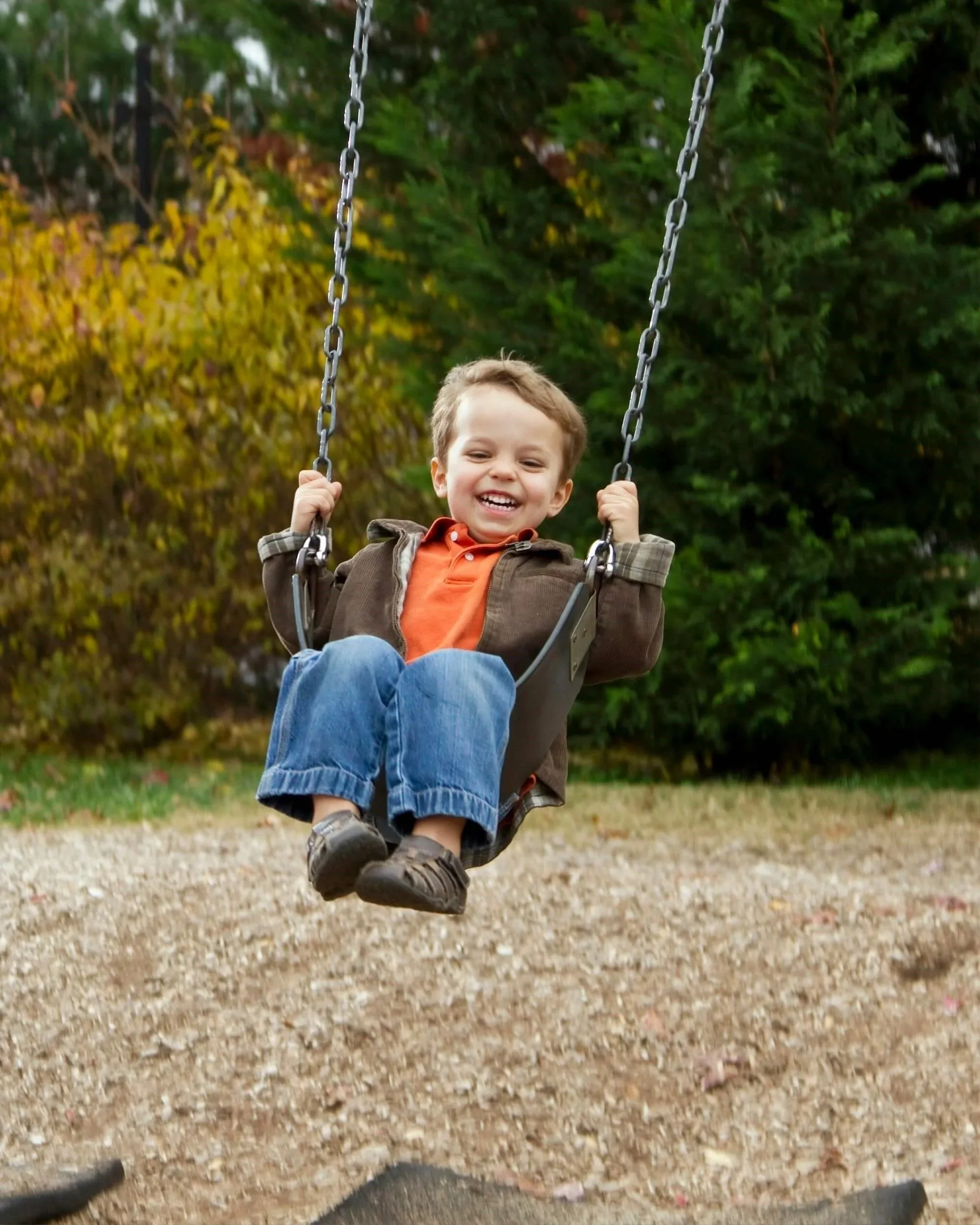 Smiling boy in brown jacket and orange shirt on swing