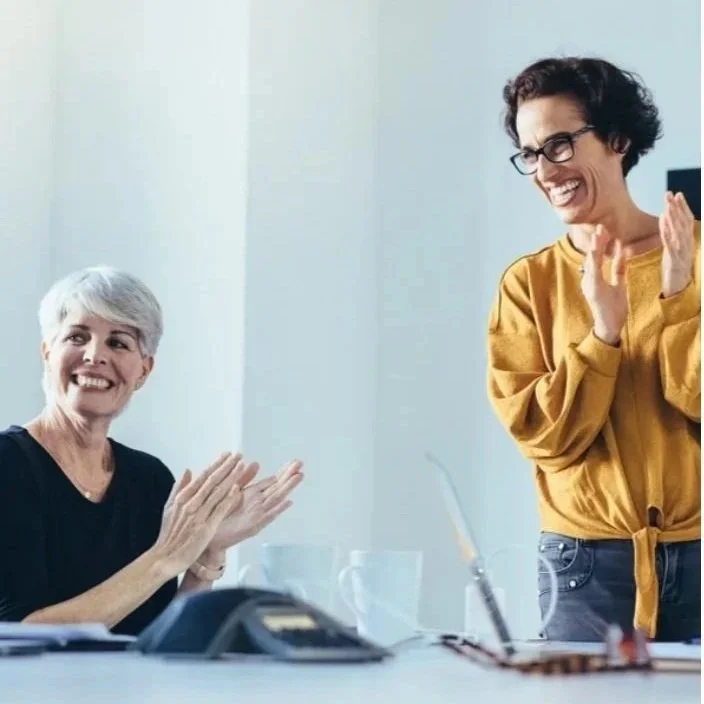 Two business women clapping looking at someone