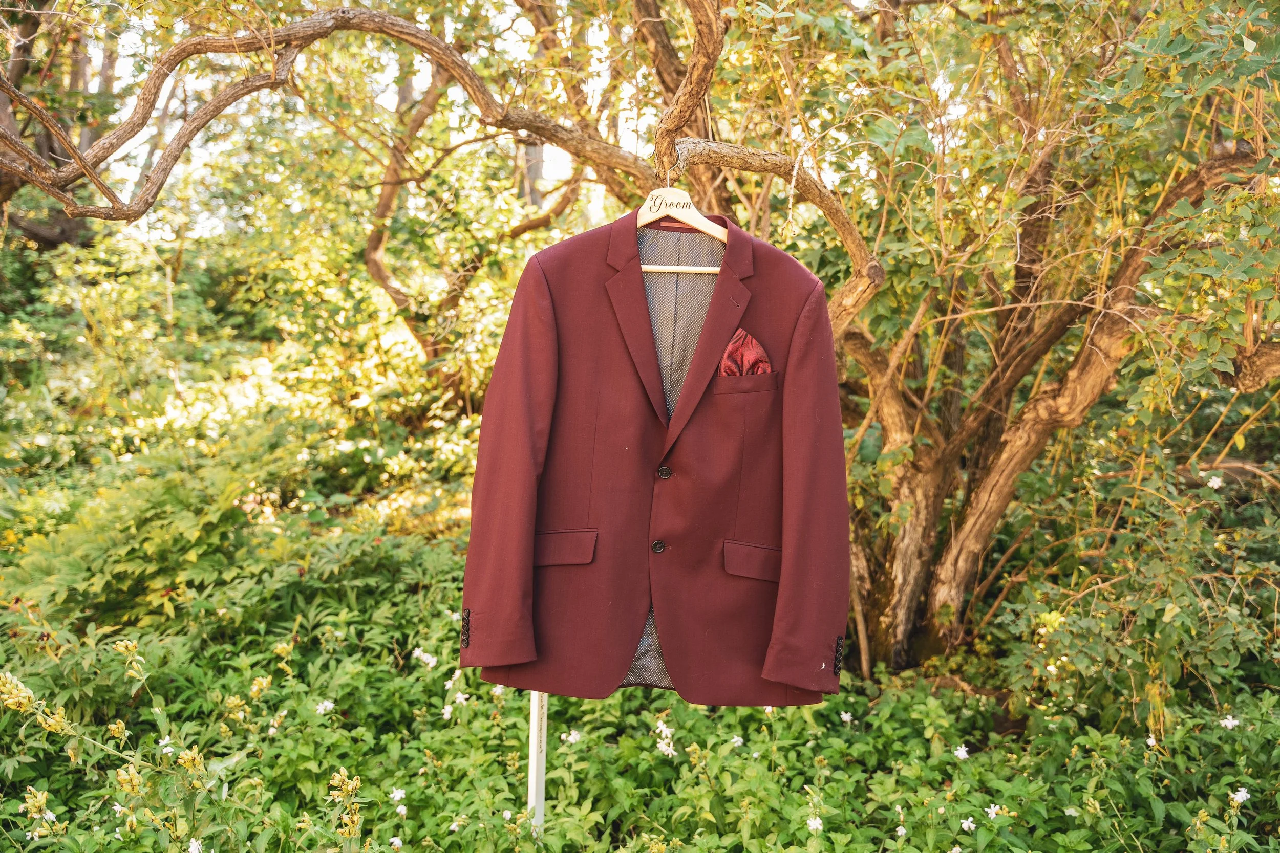 Groom Oscar's burgundy wedding suit hanging on a tree branch during getting ready Calgary