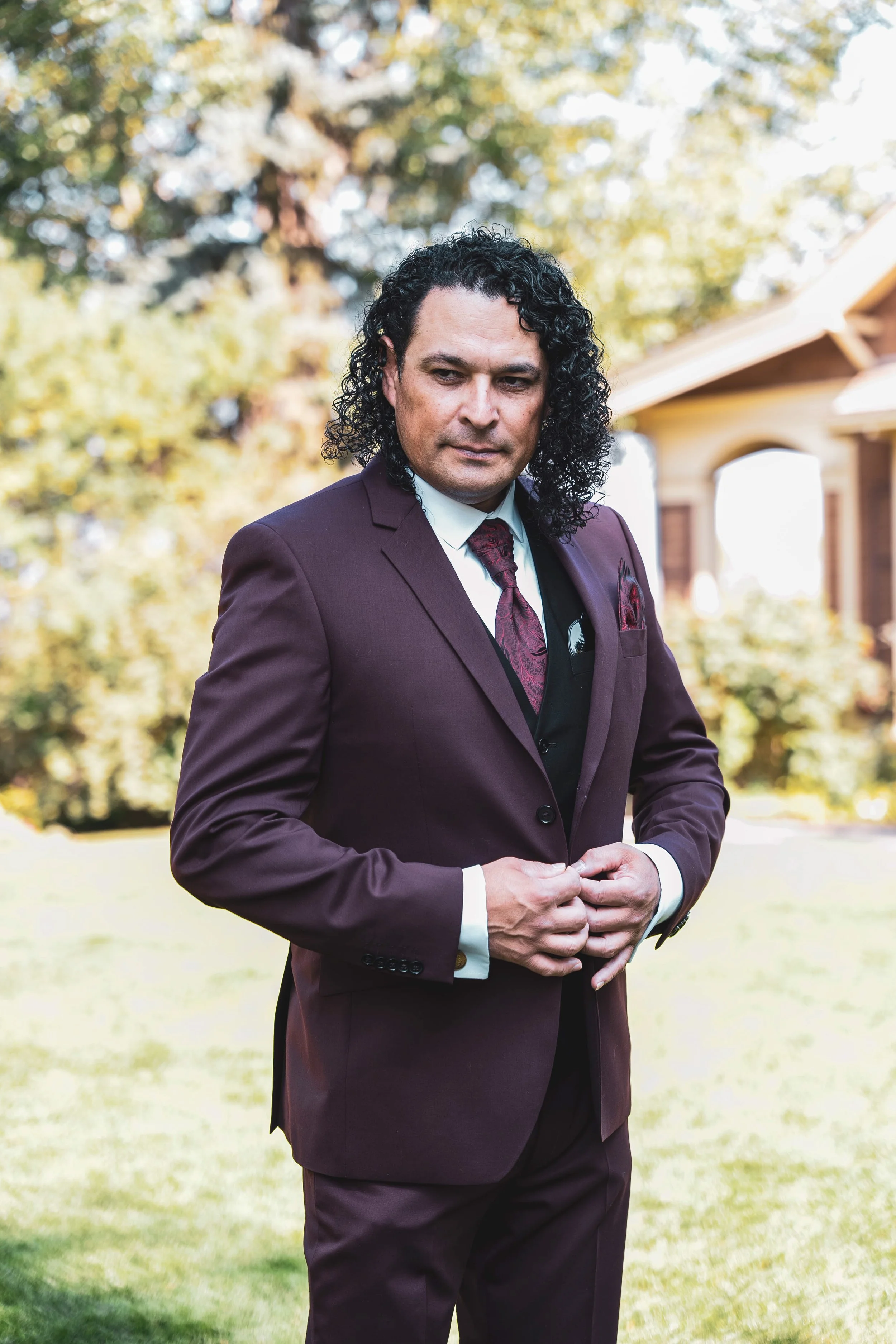 Groom Oscar putting on his burgundy suit jacket outdoors during wedding morning getting ready Calgary
