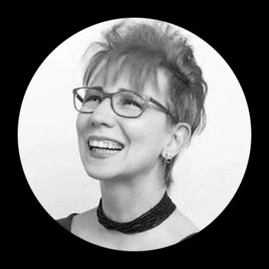 Black and white portrait of a smiling woman with short hair, glasses, and a choker necklace.