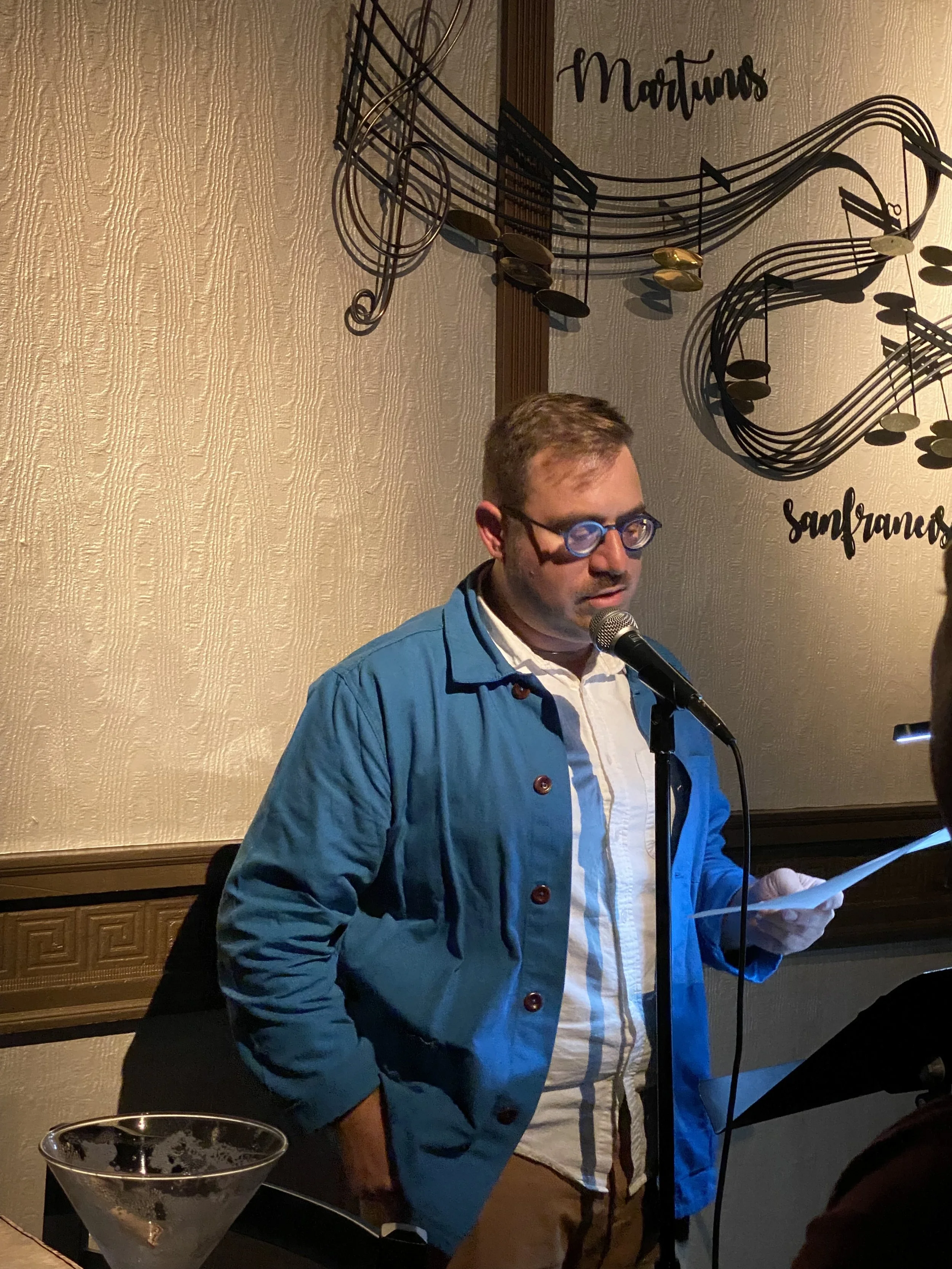 T.S. Leonard, a white person wearing a blue chore coat, reads poetry at Martuni's in San Francisco.