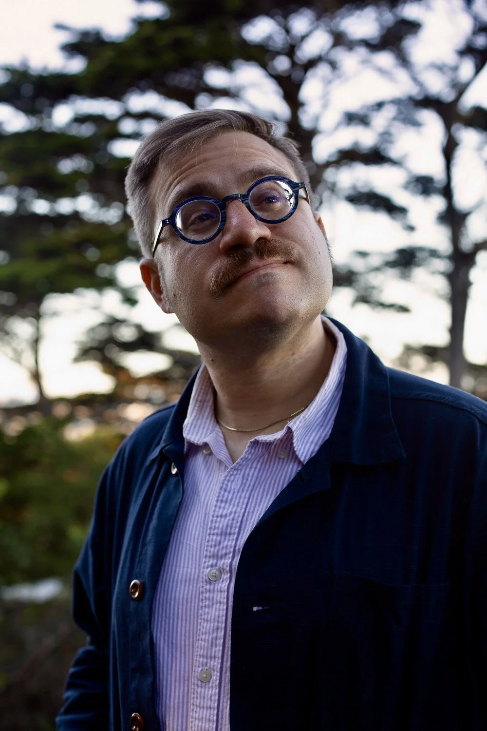 T.S. Leonard, a white person with a mustache, poses in blue glasses.