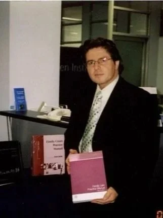 A man in a suit holding a pink book in an office setting.