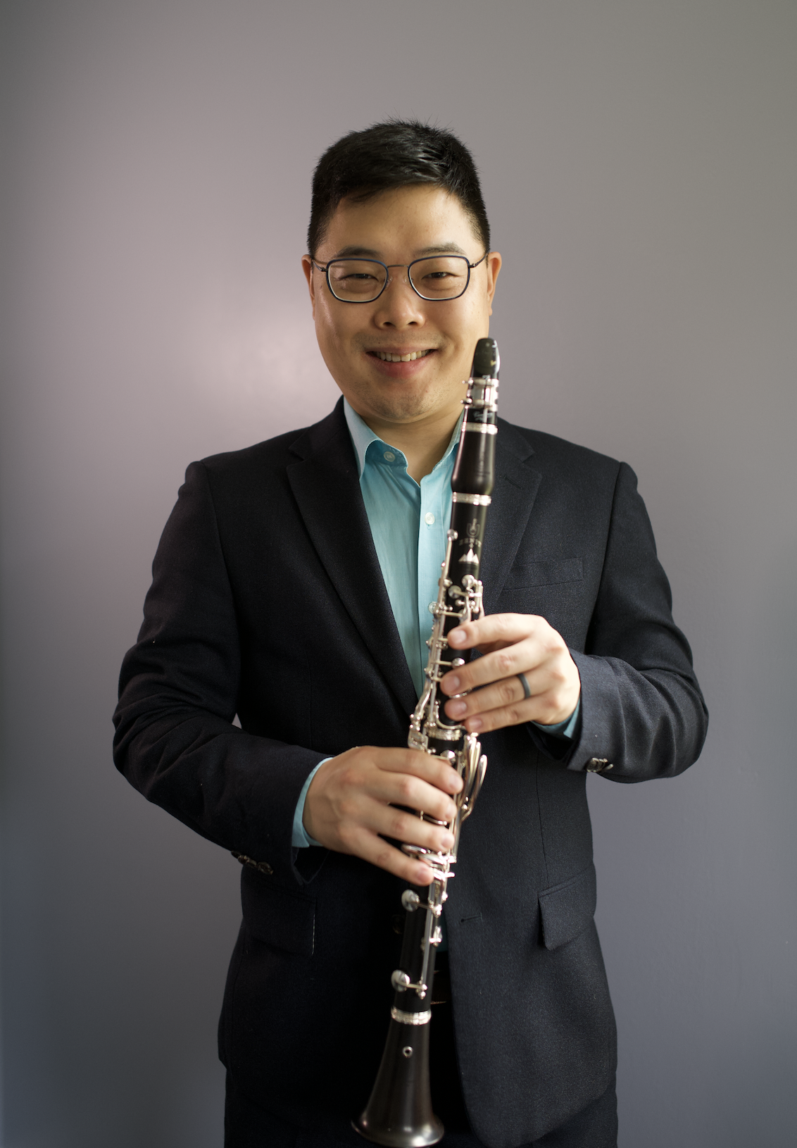A man dressed in a suit holding a clarinet and smiling at the camera.