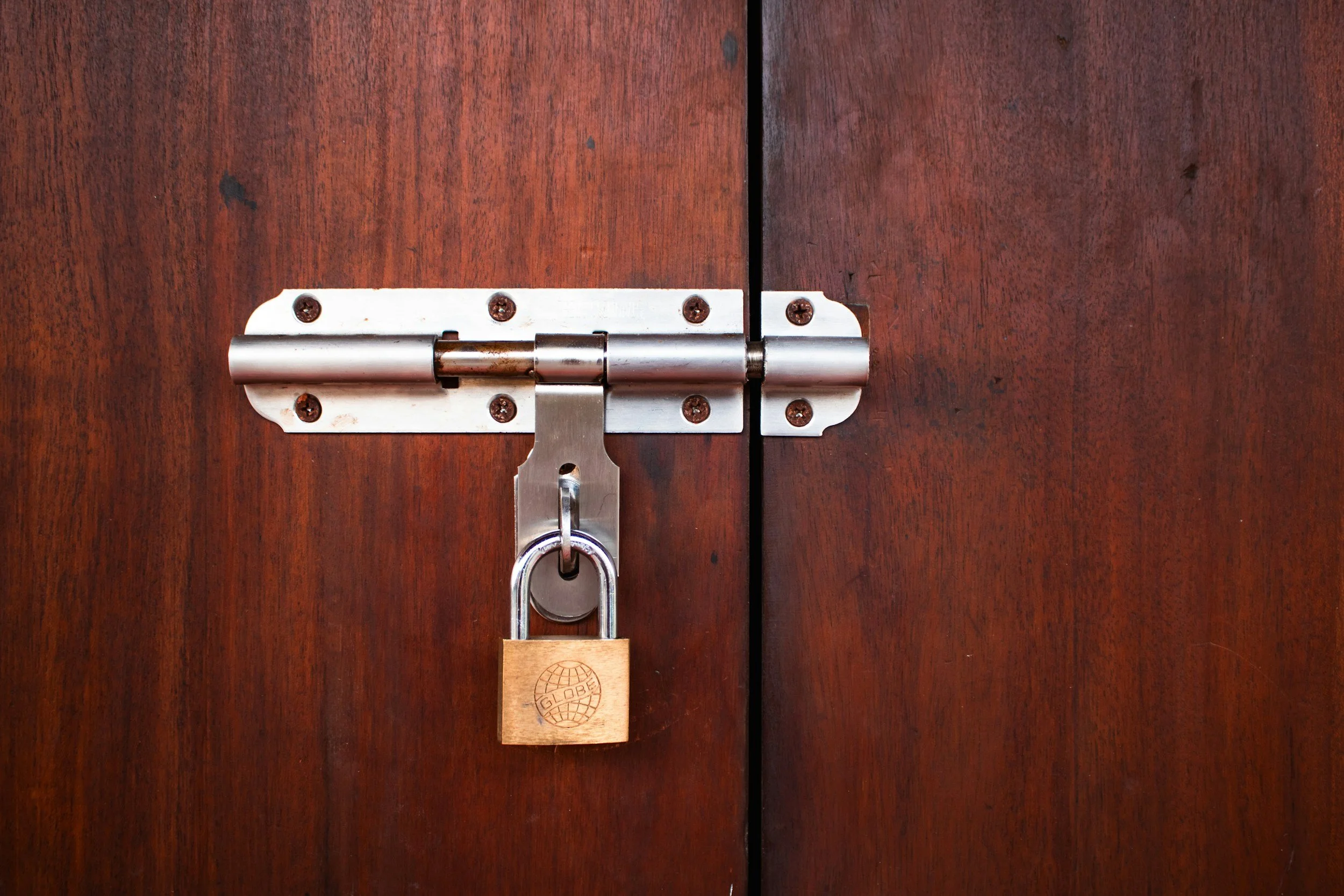 Wooden cabinet door with a metal hinge secured by a padlock.