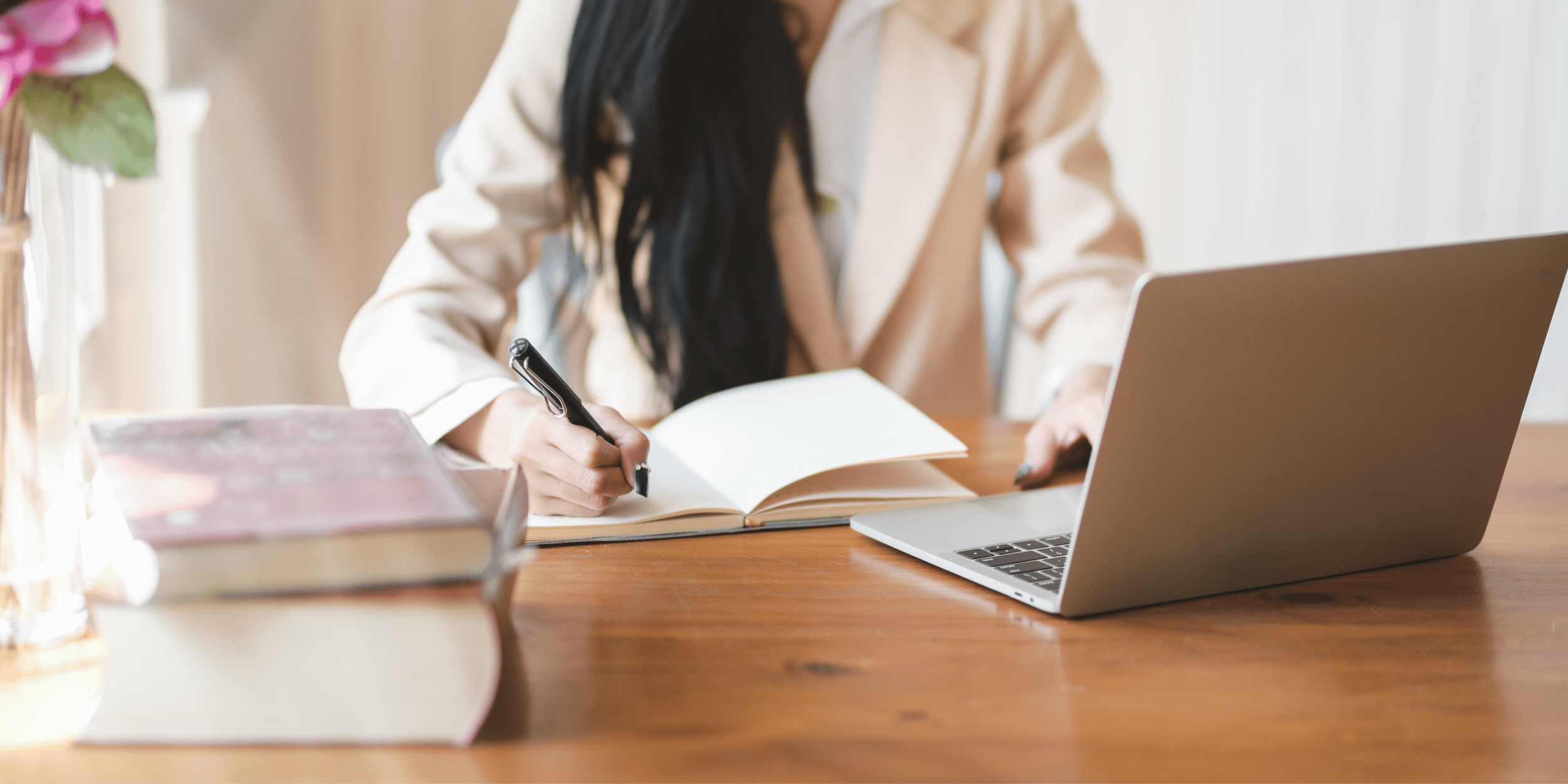 Woman at table with laptop and writing in a notebook