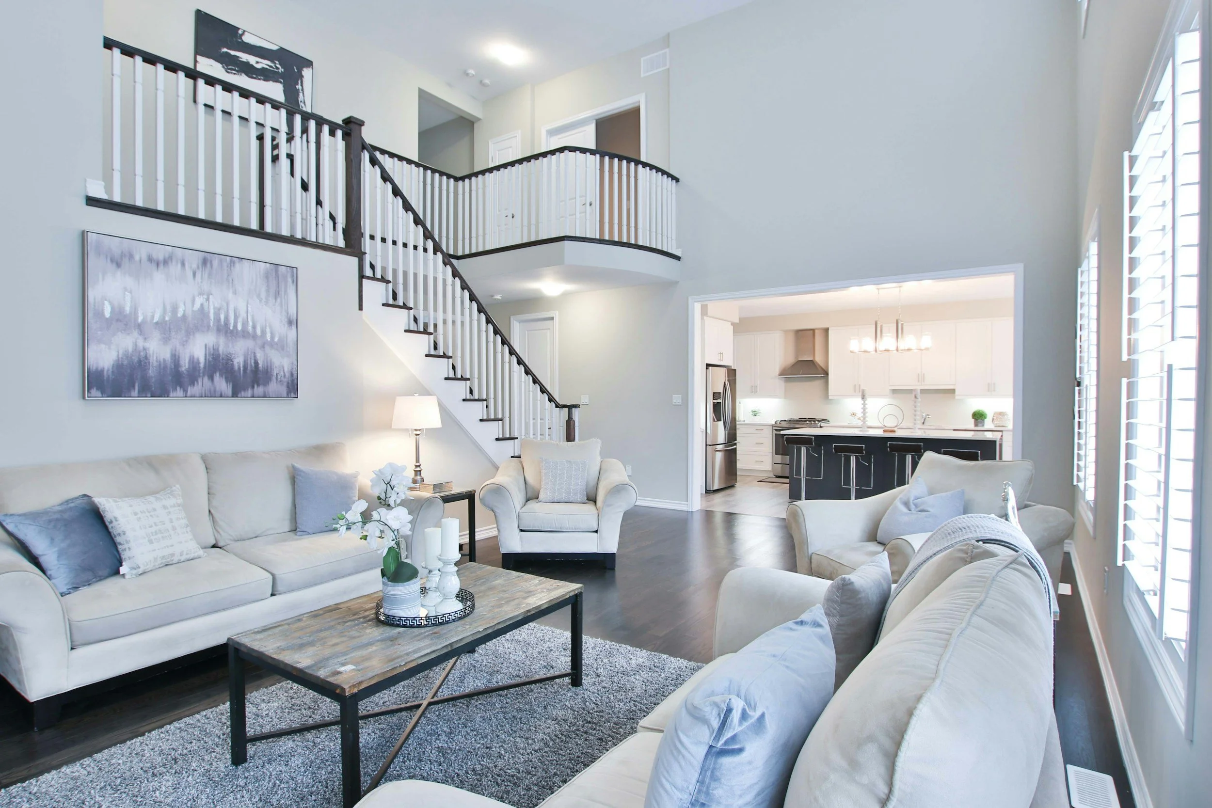 Living room with cream sofas, dark wood floors, a coffee table, and an open kitchen in the background.