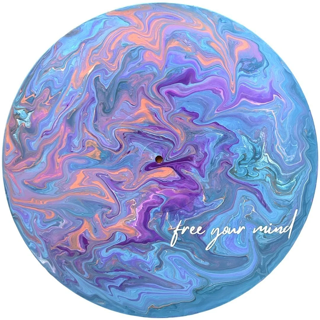 A colorful, swirling abstract pattern on a circular surface with shades of purple, blue, and peach, featuring the phrase 'free your mind' written in white cursive text.