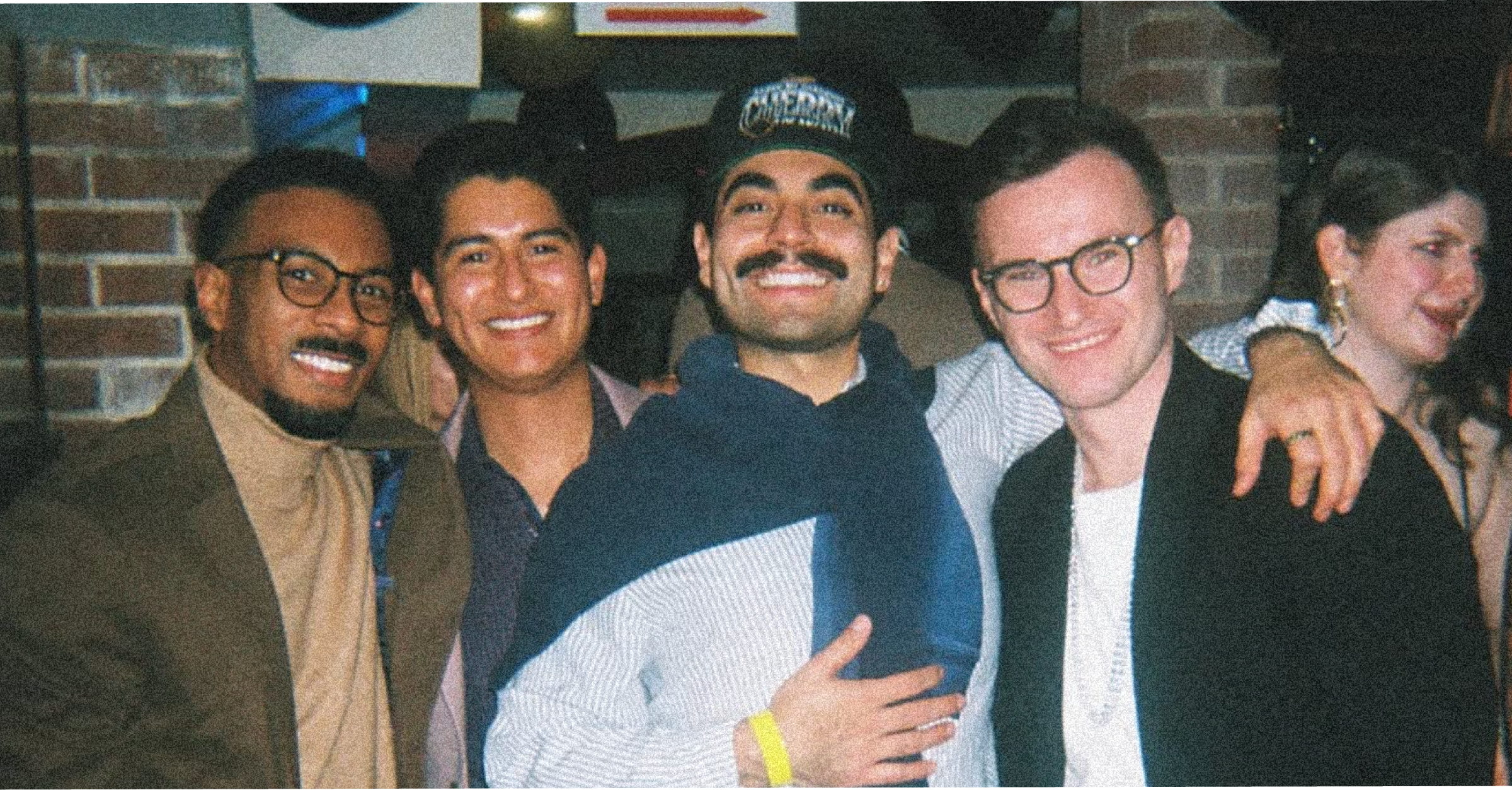 Group of friends smiling and celebrating together at Bar Sotto, with brick walls in the background.
