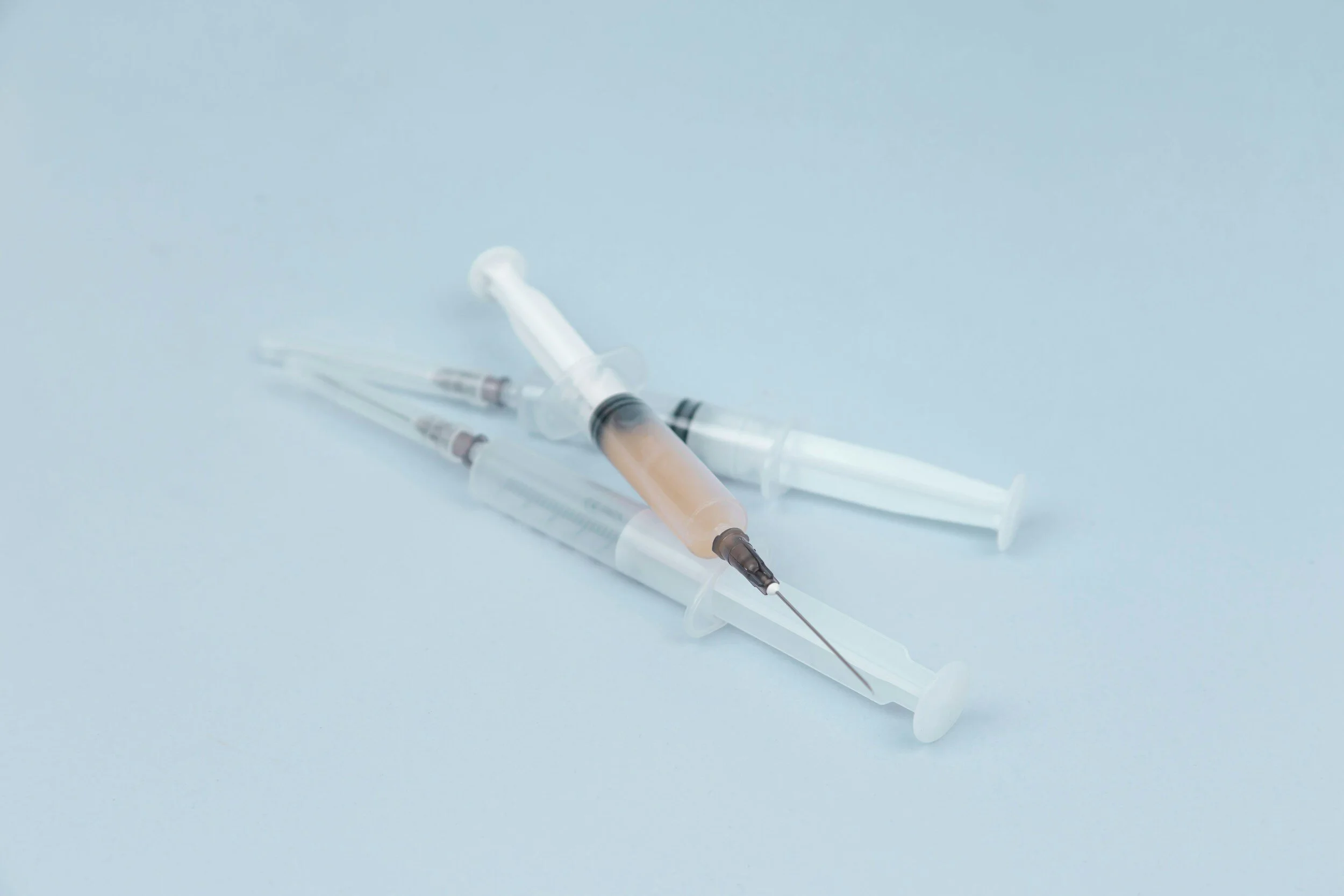 Three syringes, one filled with a brownish liquid, on a light blue surface.