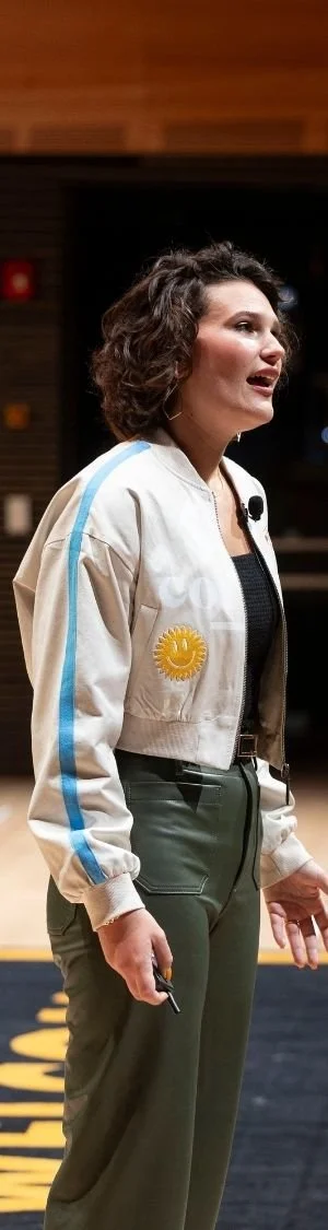 Lindsay mid-speech on stage at the Welcome Conference wearing a 321 Coffee bomber jacket.
