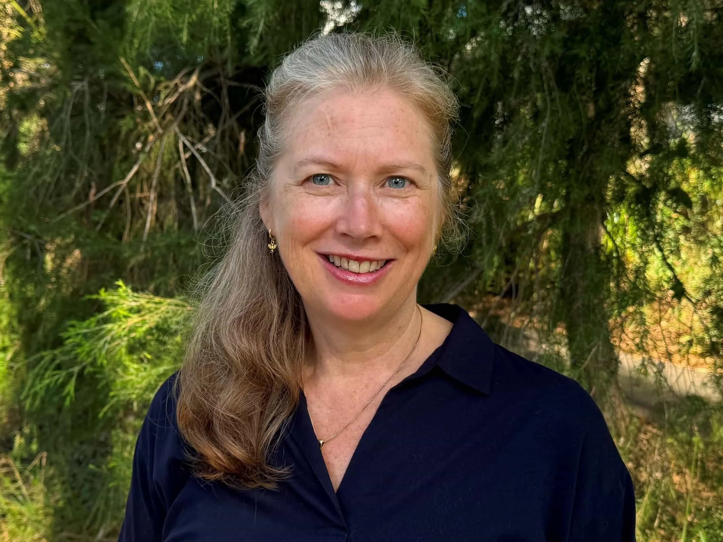 Michelle Player in a navy top smiling outdoors in front of green leafy trees in Bella Vista.