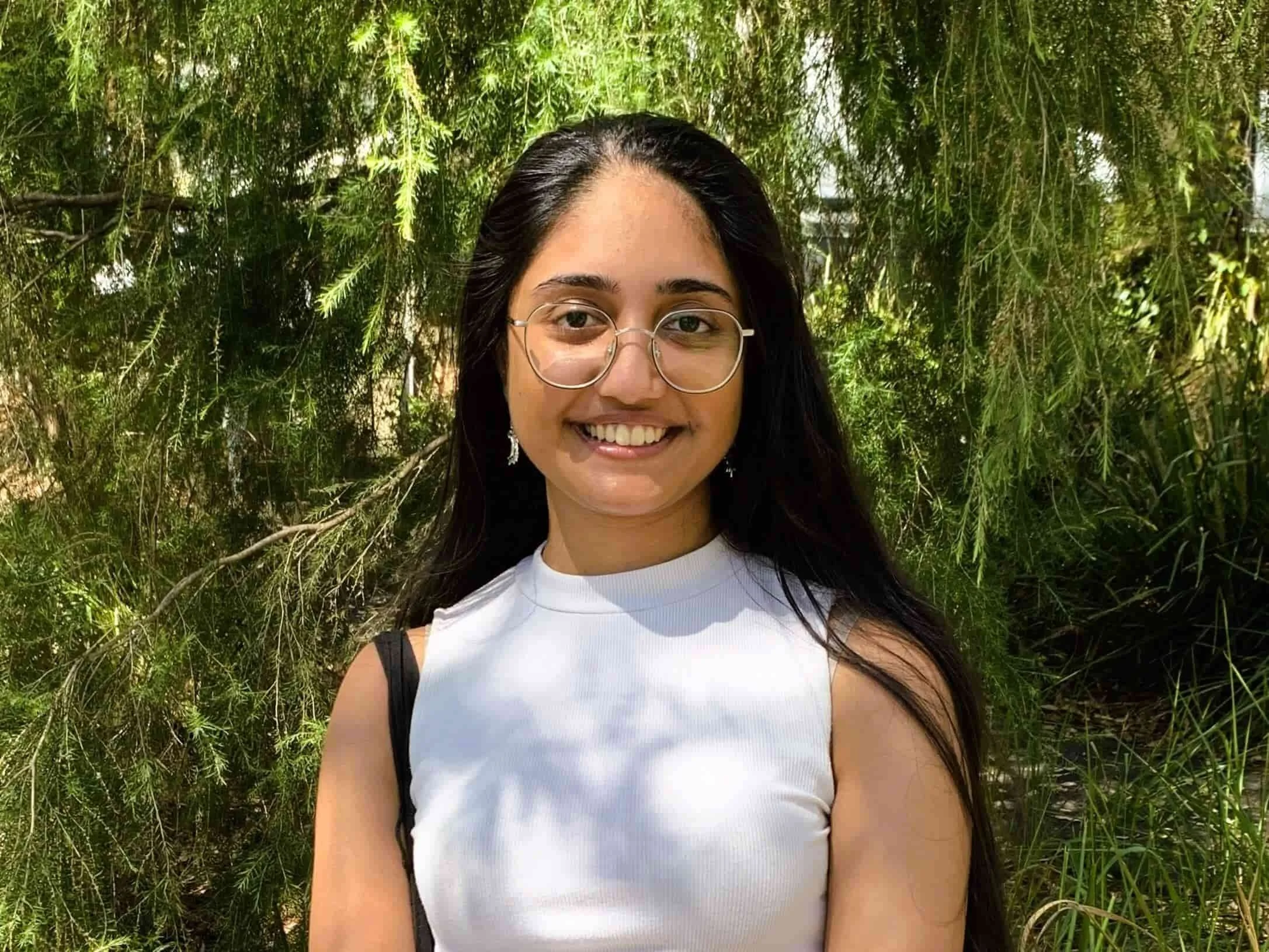Anushka Kapdi in a sleeveless white top smiling outdoors in front of green leafy trees in Bella Vista.