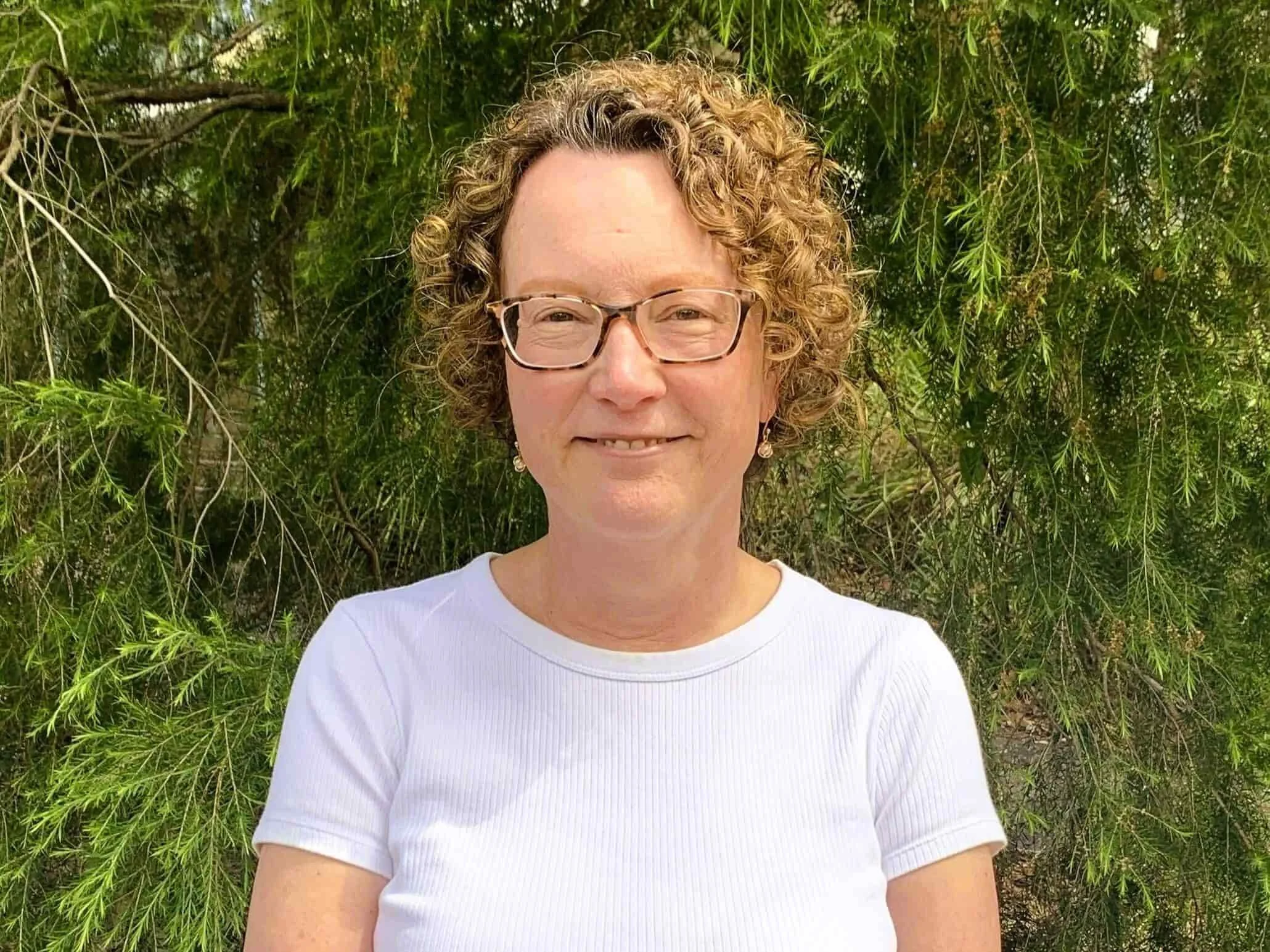 Dianne Swinsburg in a white top smiling outdoors in front of green leafy trees in Bella Vista.