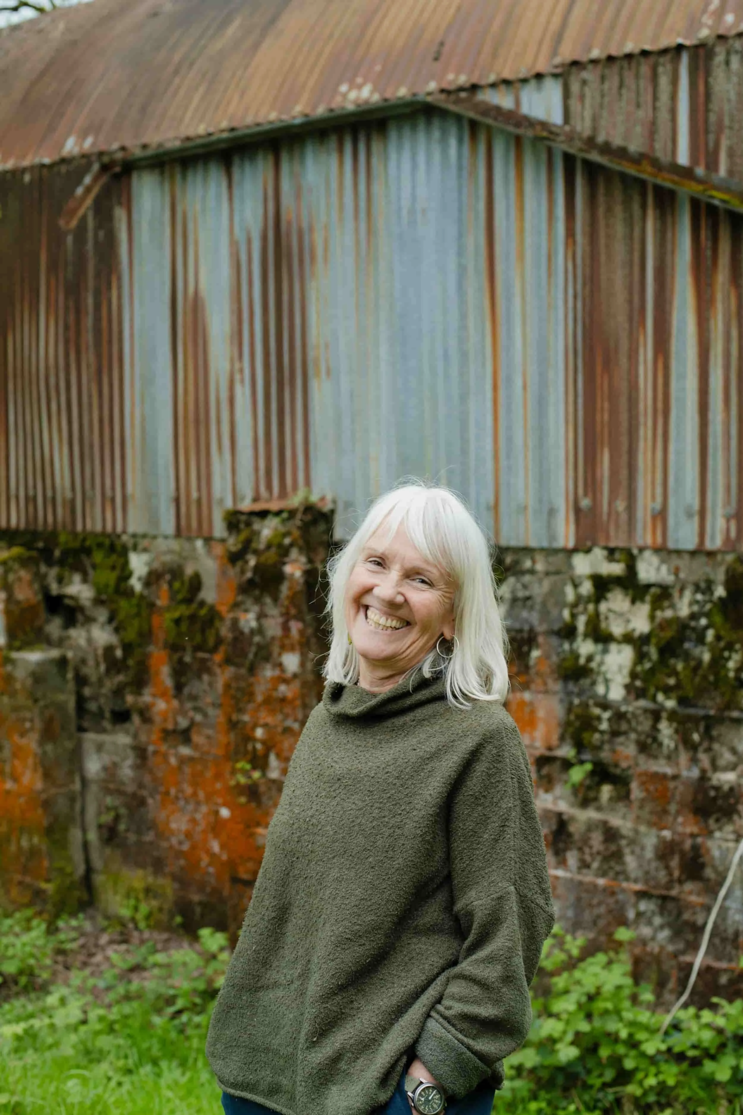 Older woman with a joyful expression standing in front of a rusty fence