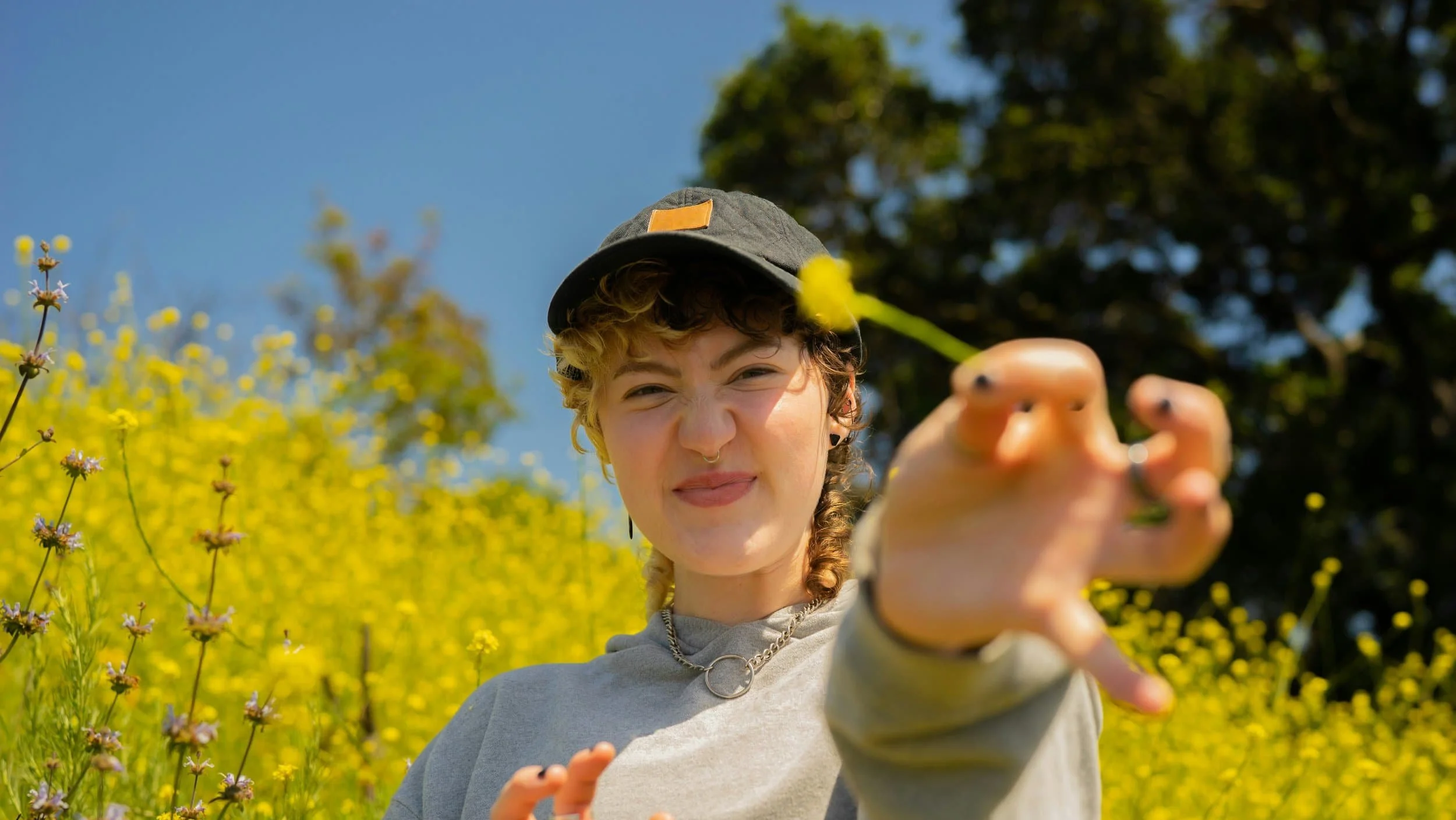 A teenager in a flower field holding out a daisy