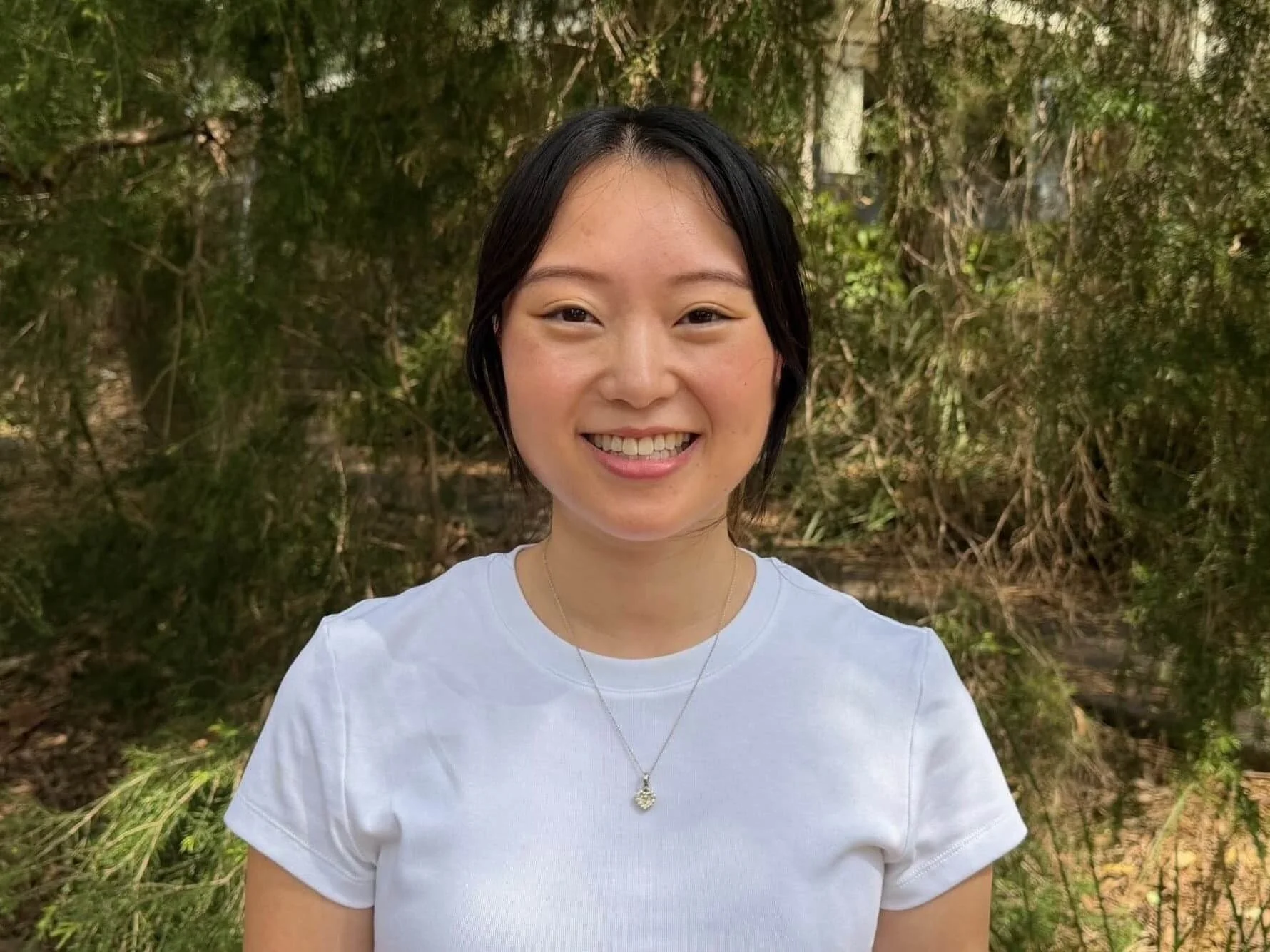 Monica Kim in a white top smiling outdoors in front of green leafy trees in Bella Vista.