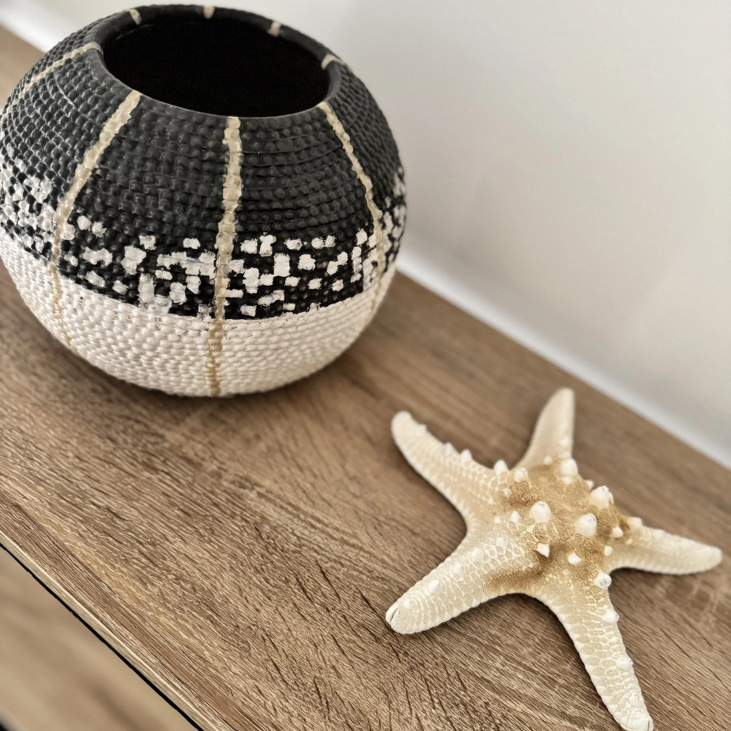A black and white decorative vase with geometric patterns next to a beige starfish on a wooden surface.