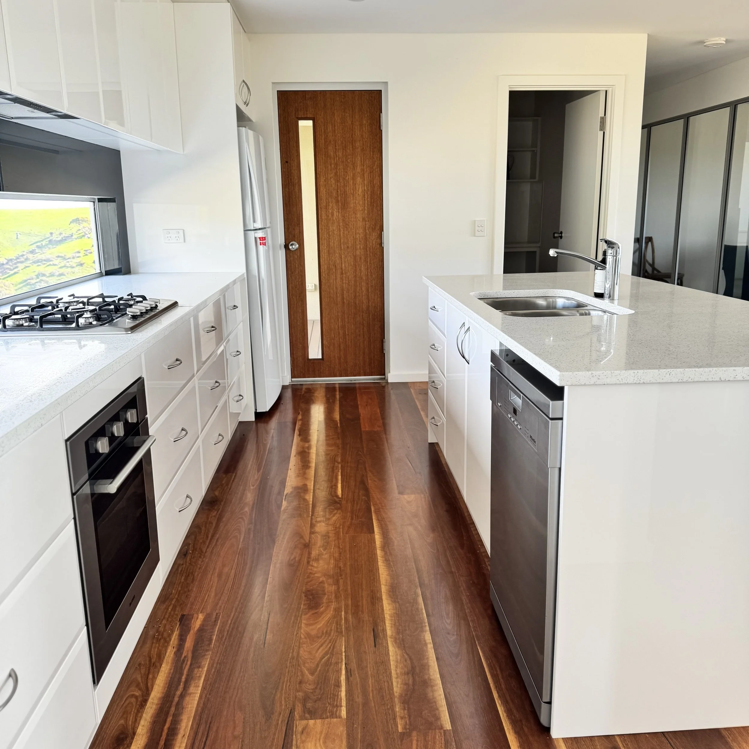 Modern kitchen with white cabinets, a kitchen island with a sink, wooden flooring, and a wooden door with a mirror panel.
