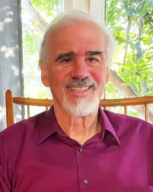 A close-up of Jules Confino, LMFT, sitting in front of a window with green trees outside.
