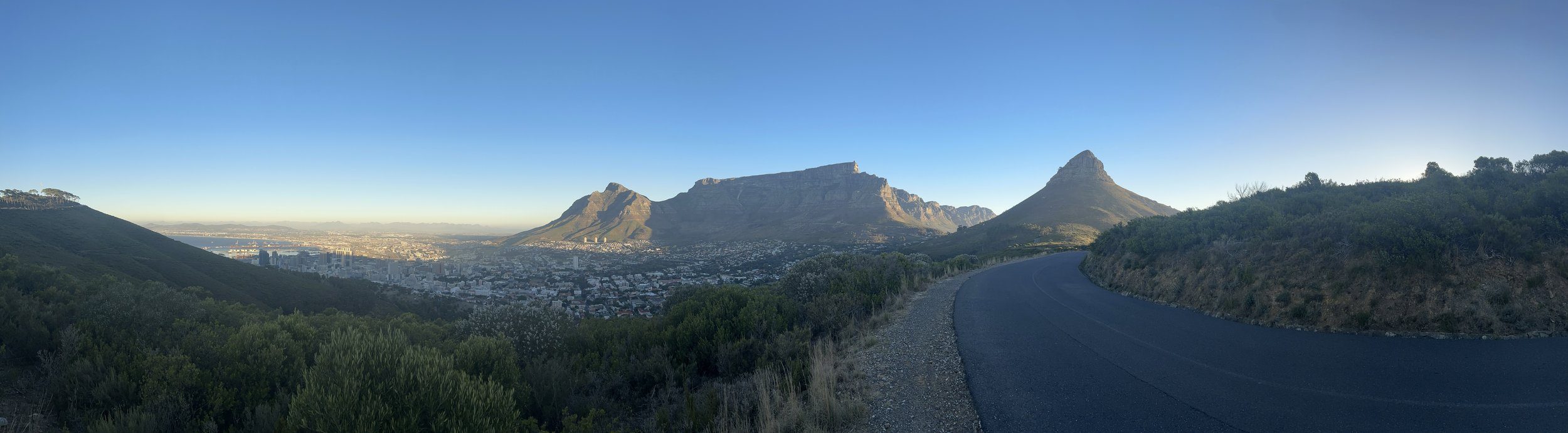 Panoramic view of Cape Town with Table Mountain, Lion's Head, and cityscape under a clear blue sky.