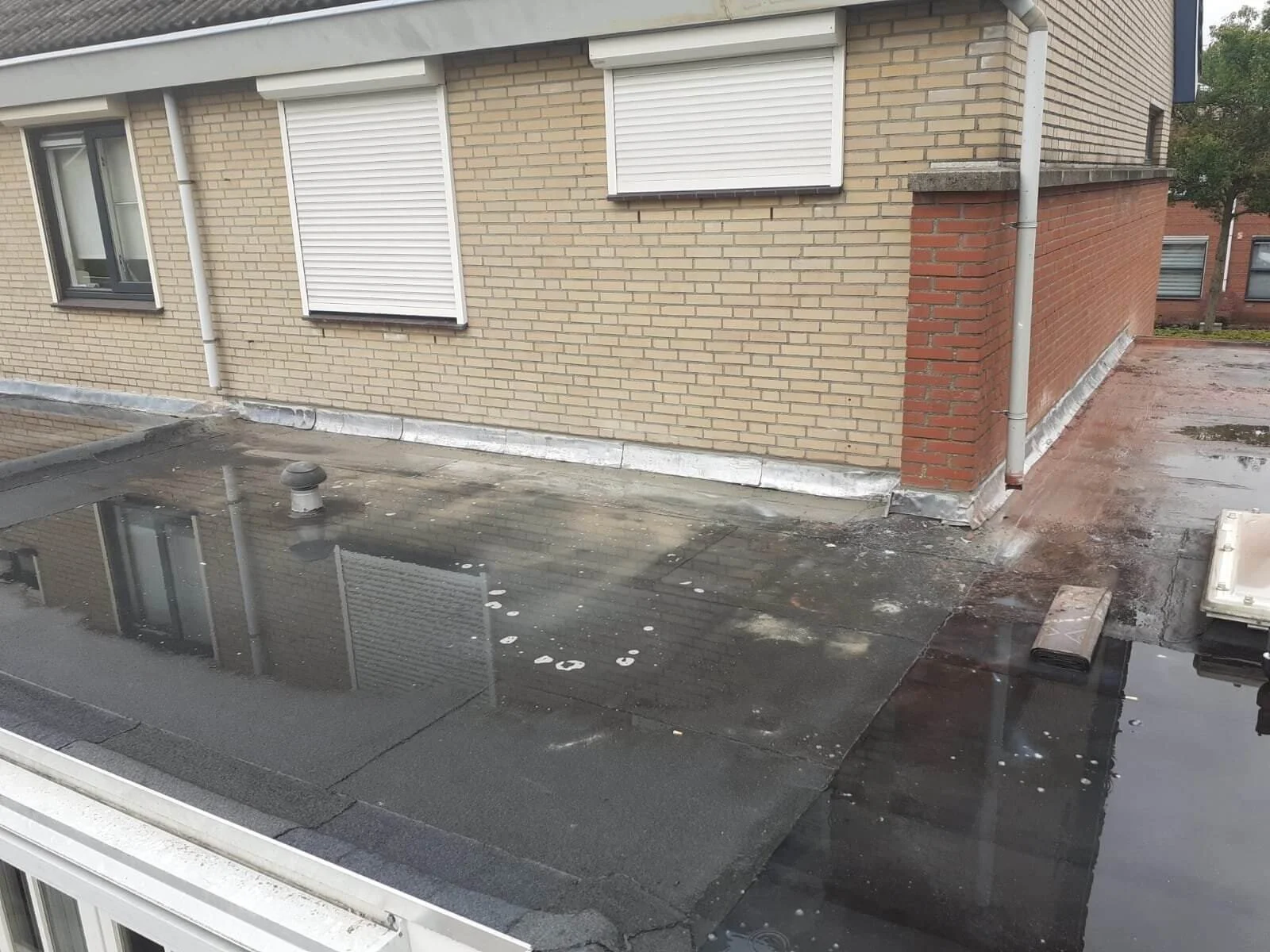 Waterplas op een plat dak van een gebouw, wat wijst op mogelijke afvoerproblemen.